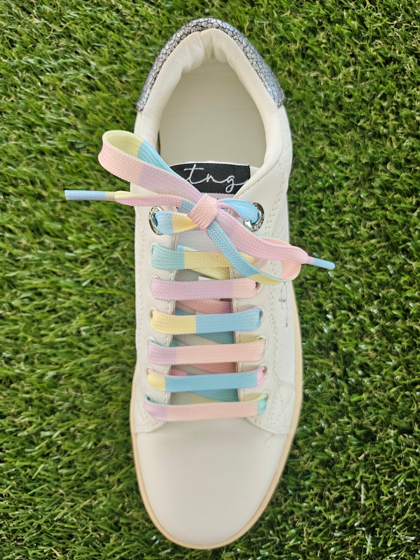 White sneaker with colorful shoelaces on a grass background