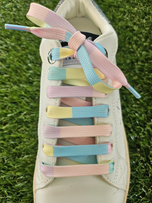 Pastel-colored shoelaces on a white sneaker against a grass background