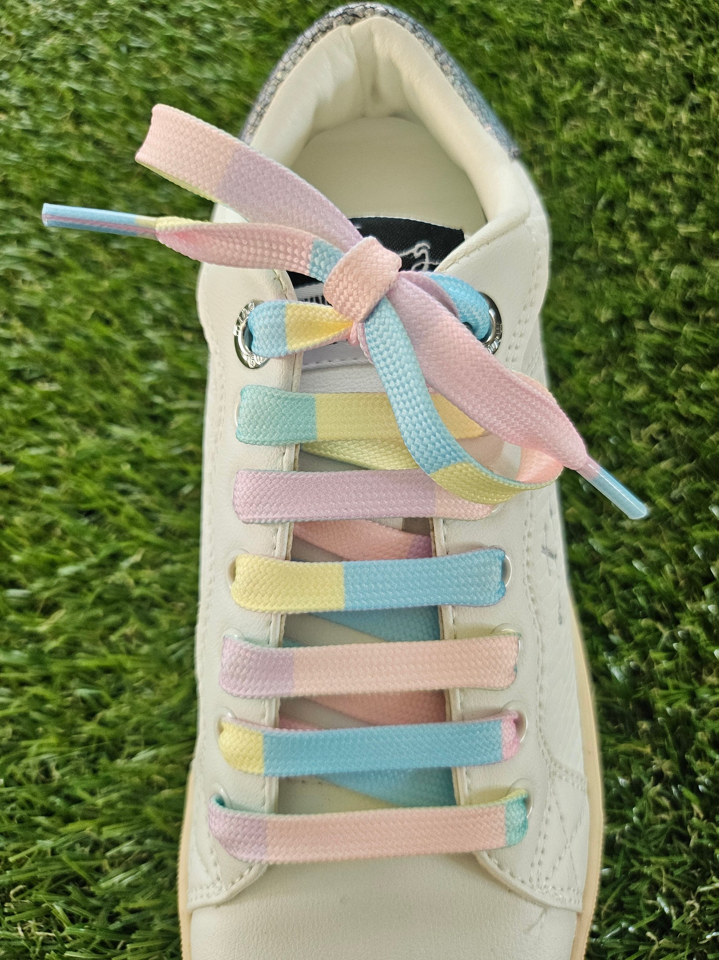 Pastel-colored shoelaces on a white sneaker against a grass background