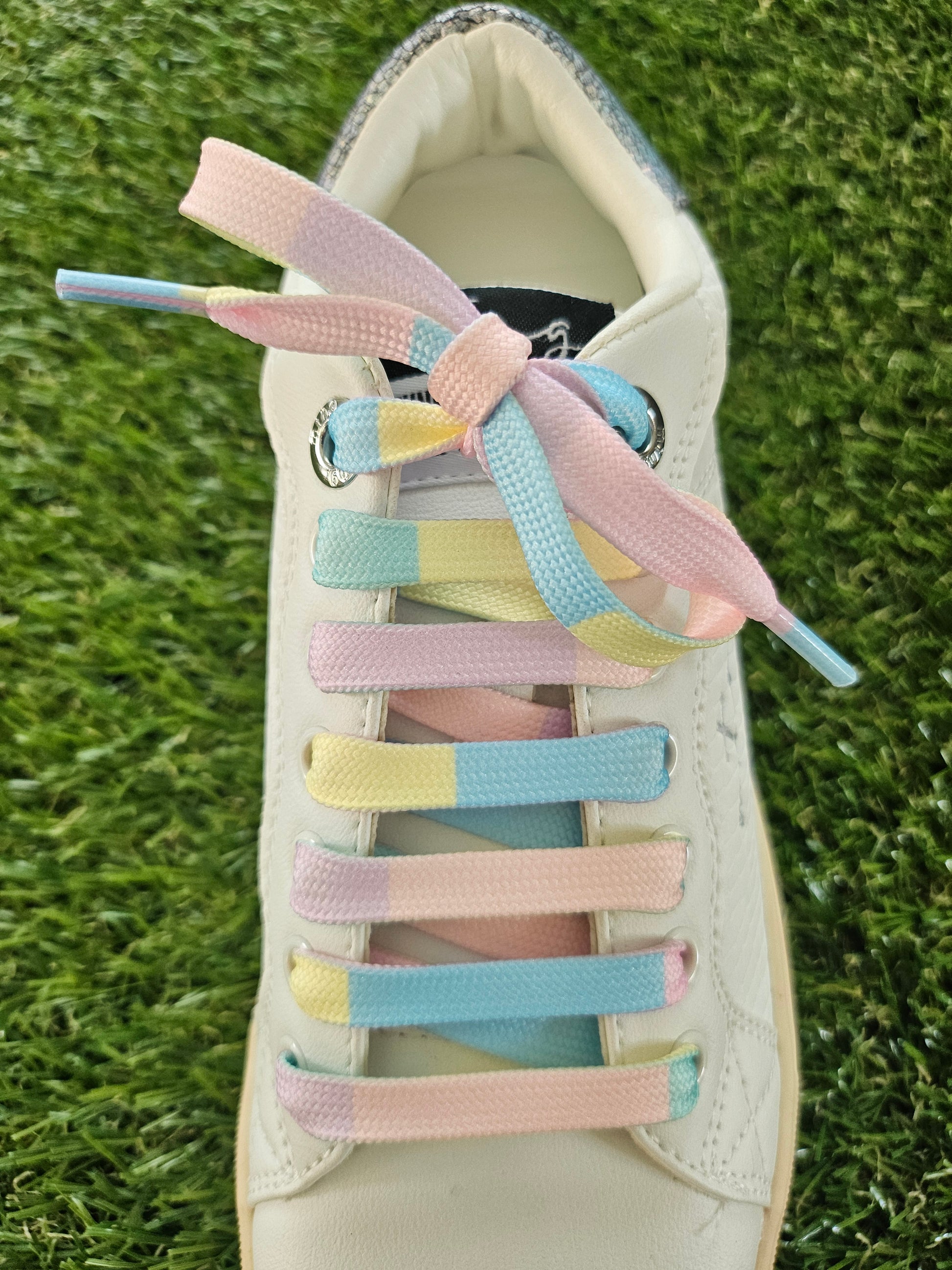 Pastel-colored shoelaces on a white sneaker against a grass background