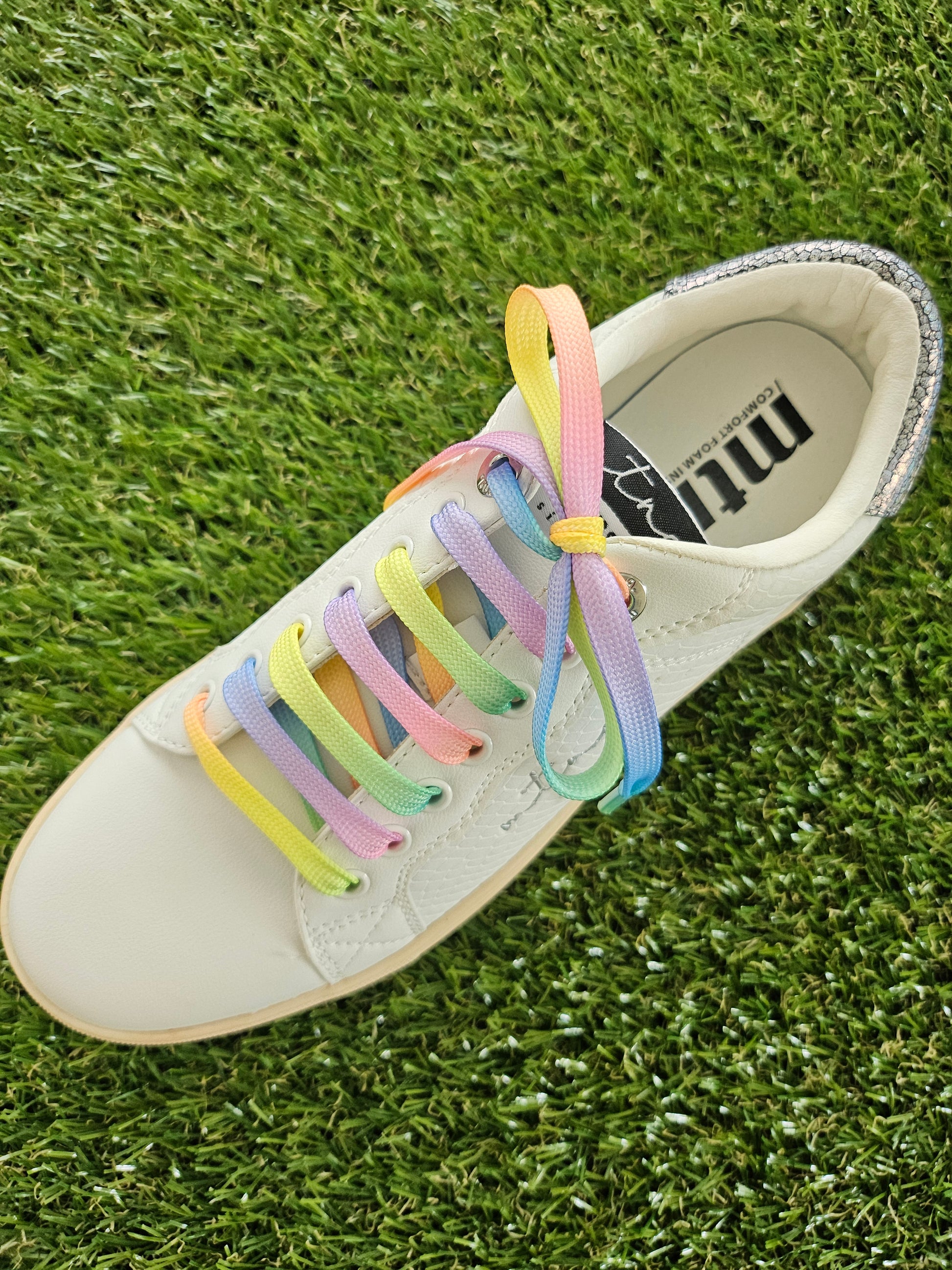 White sneaker with colorful shoelaces on a grass background