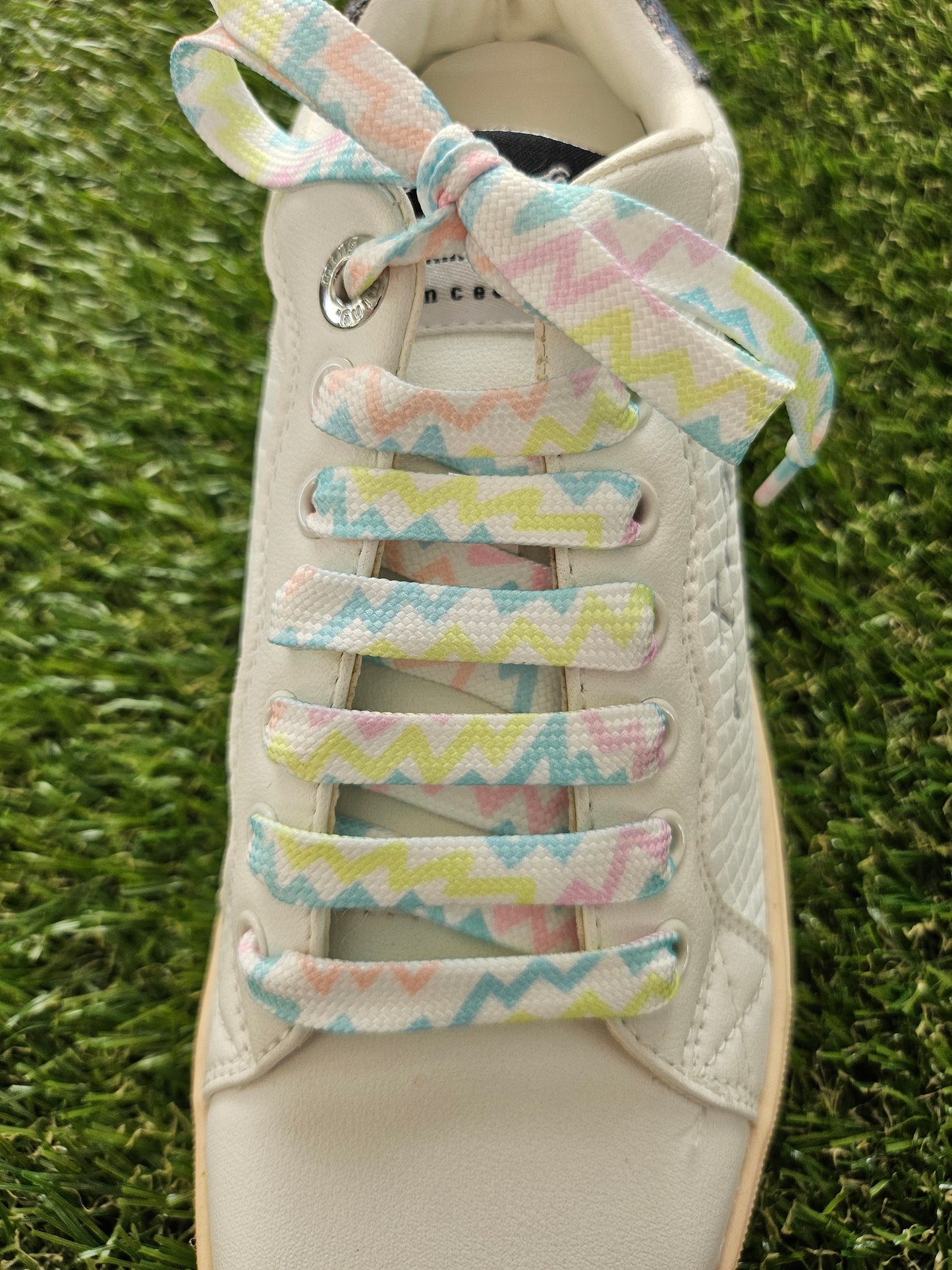 White sneaker with colorful zigzag-patterned shoelaces on a grass background