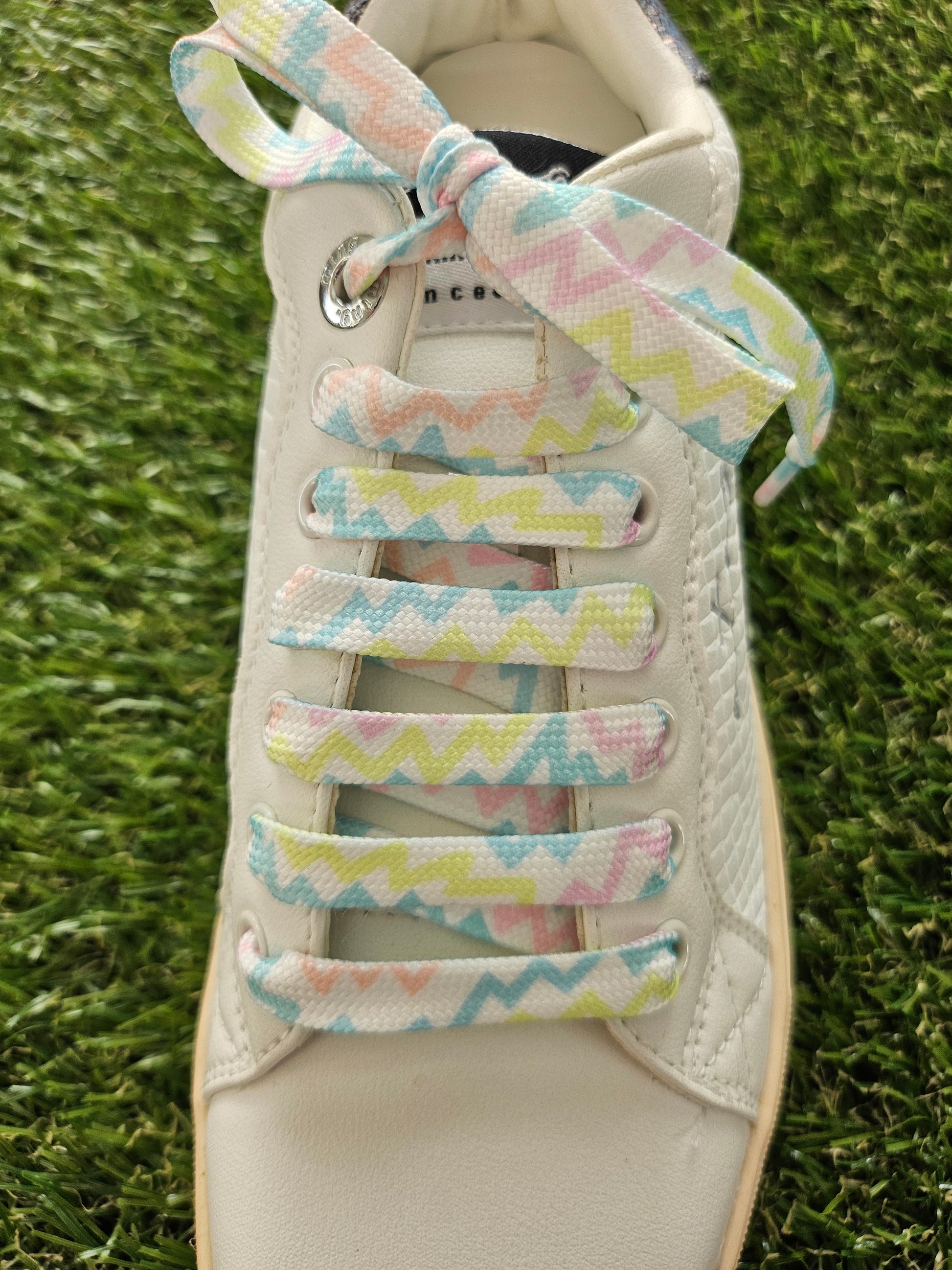 White sneaker with colorful zigzag-patterned shoelaces on a grass background