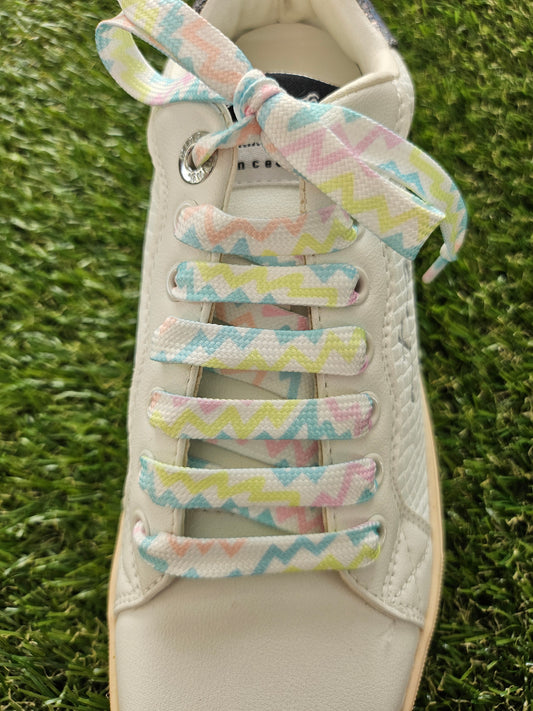 White sneaker with colorful zigzag-patterned shoelaces on a grass background