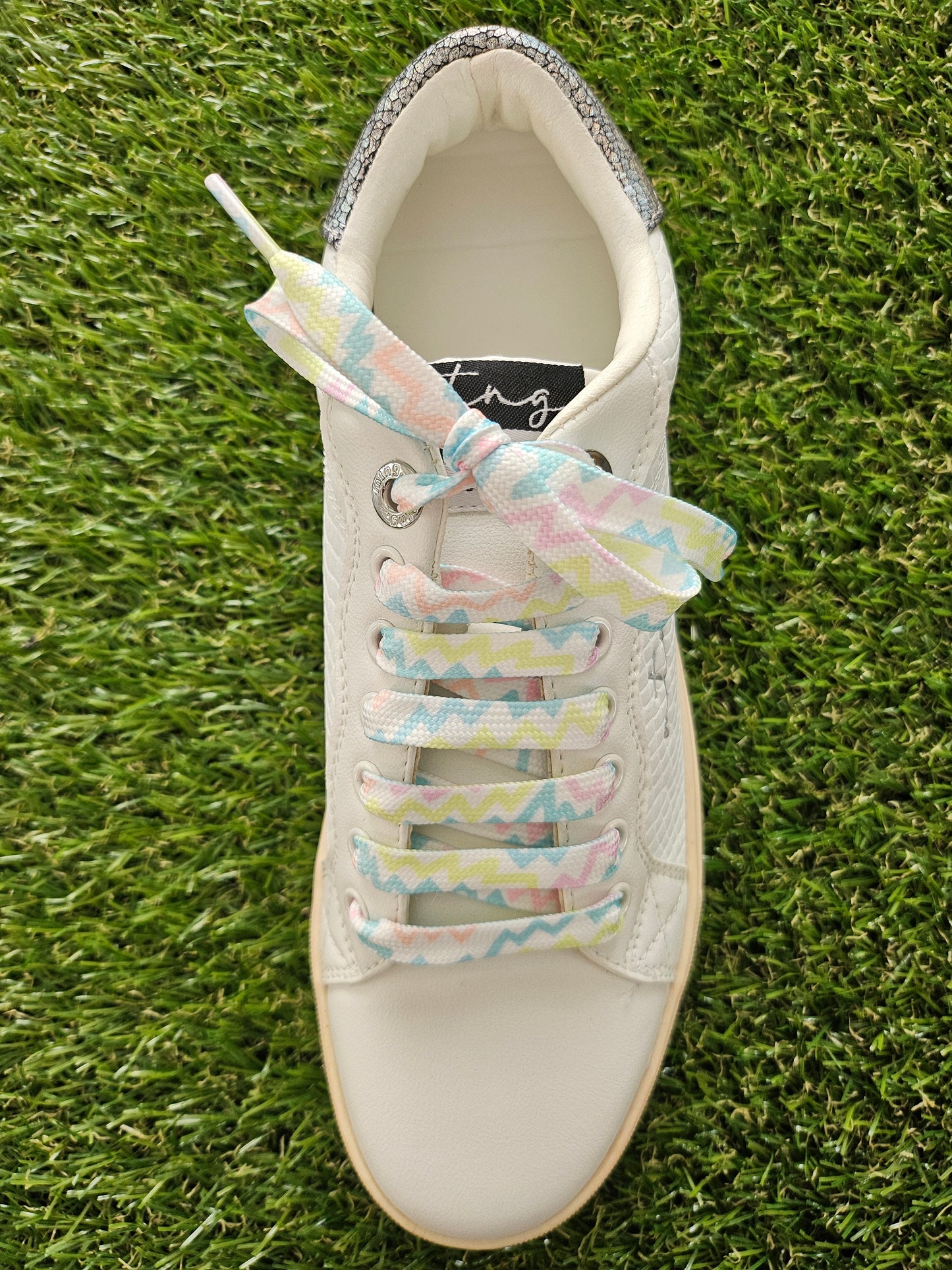 White sneaker with colorful shoelaces on a grass background