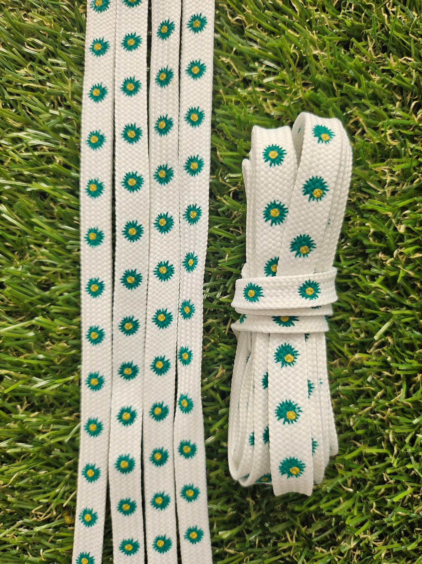 White shoelaces with pine green floral pattern on grass