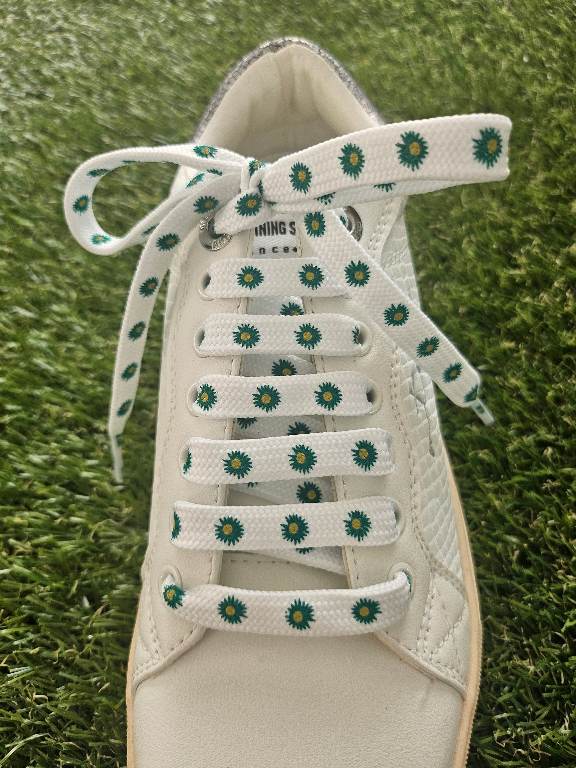 White sneaker with green floral patterns on laces on grass