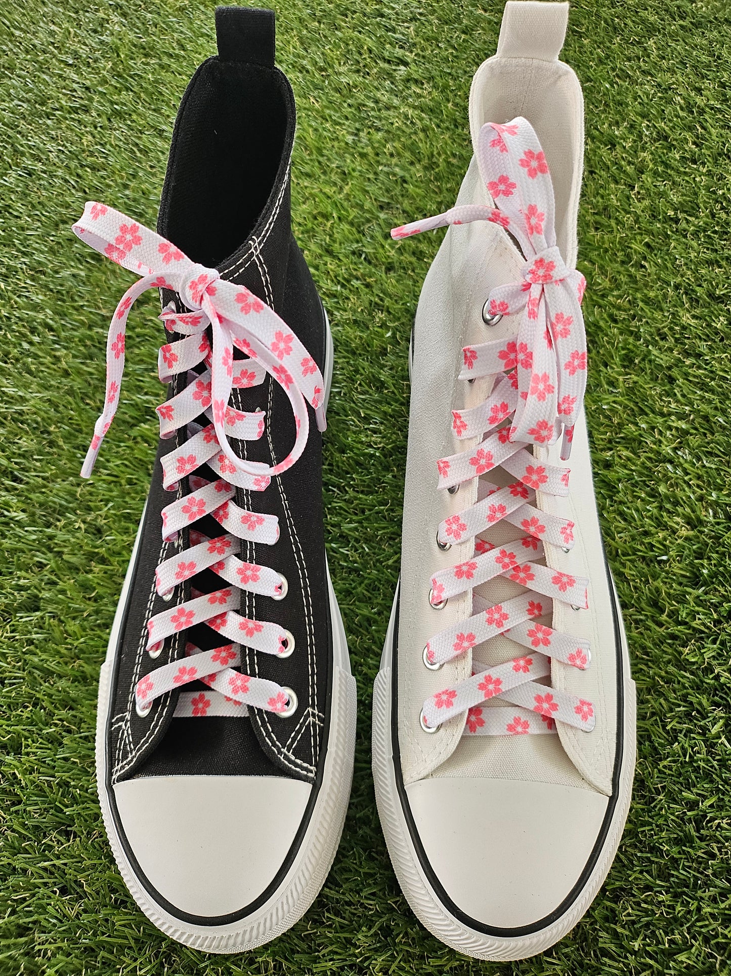 White and black sneakers with pink floral laces on a grass background