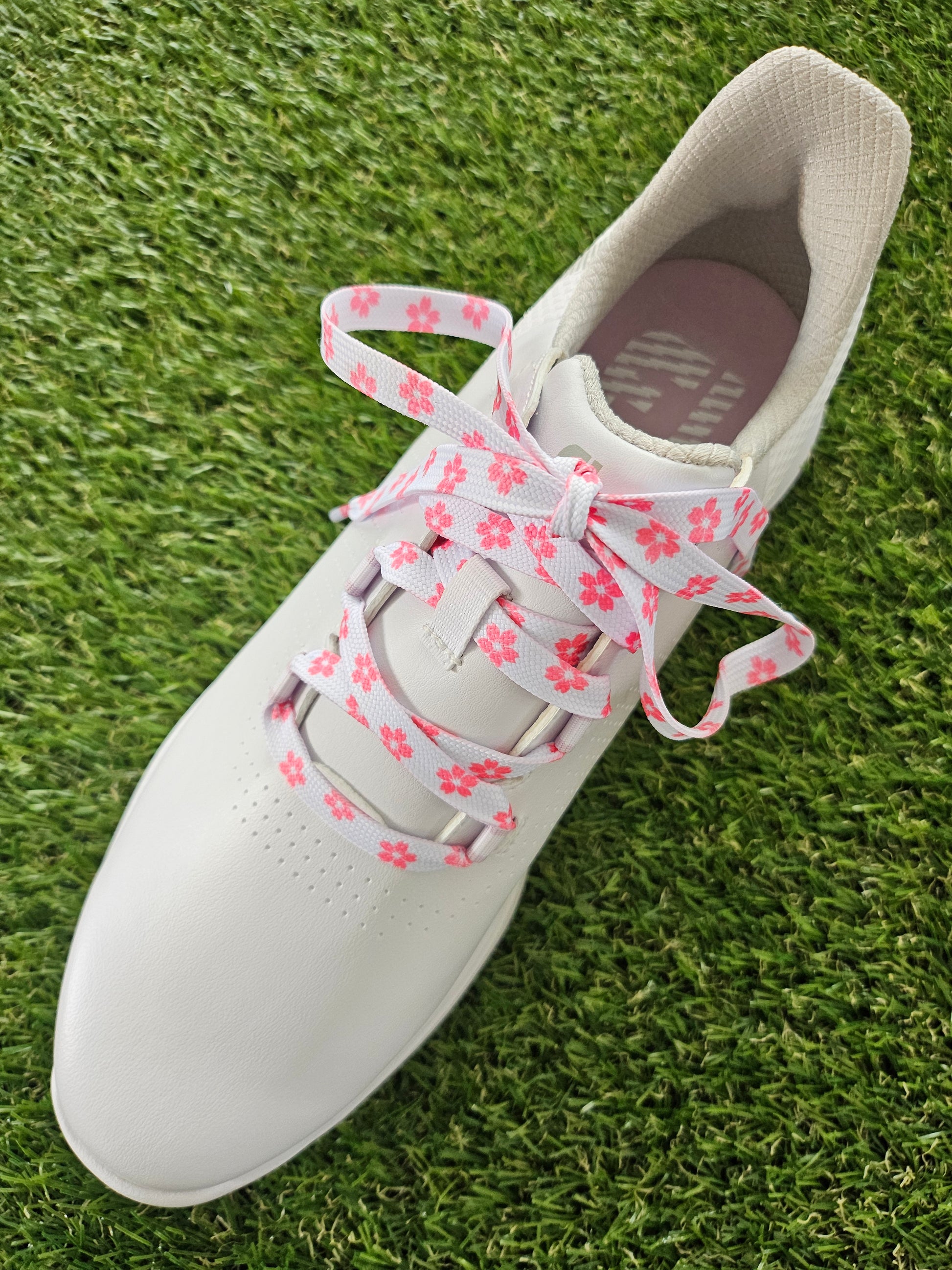 White ladies golf shoe with pink floral laces on a grass background