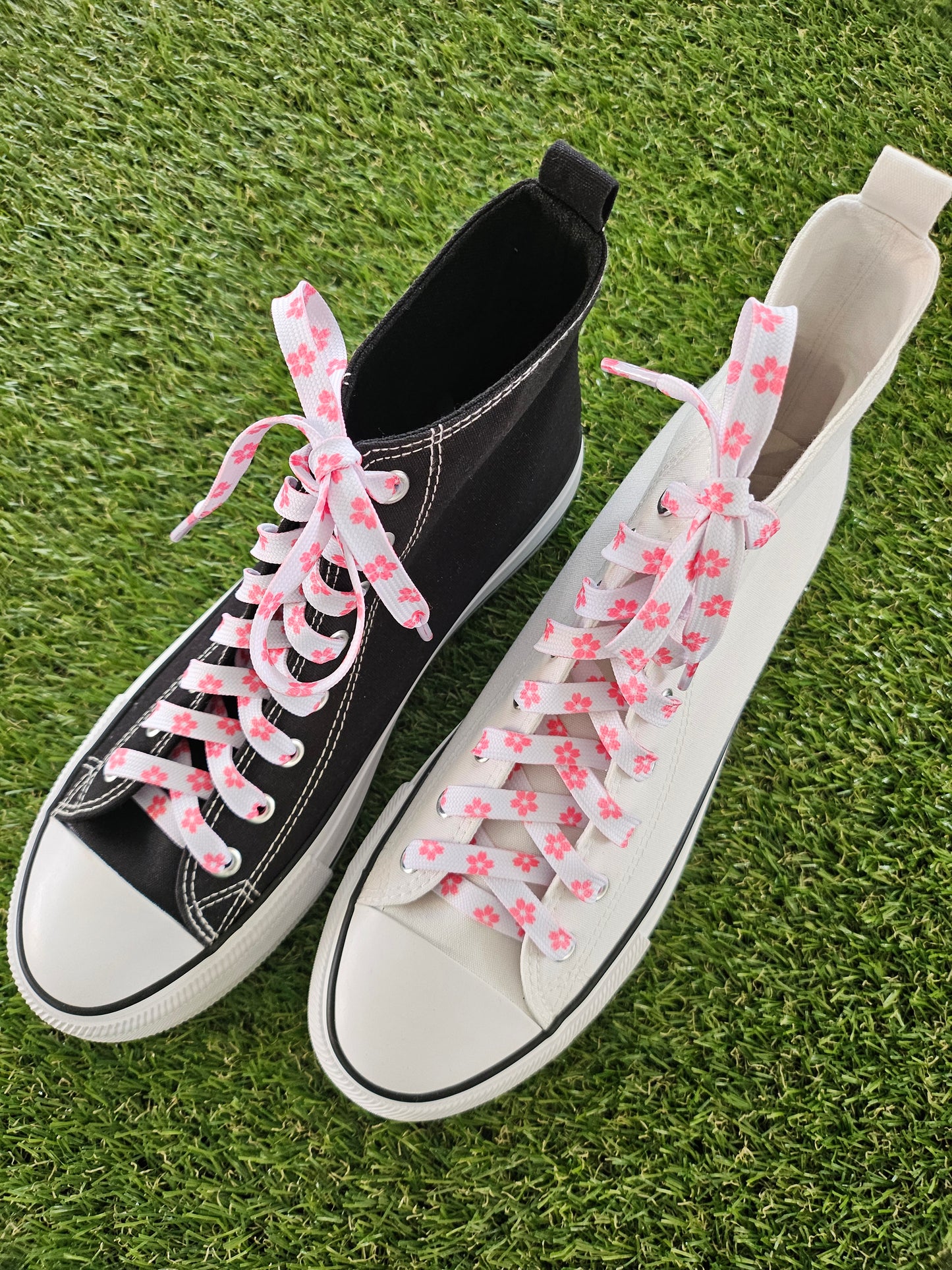 Black and white sneakers with pink floral laces on grass