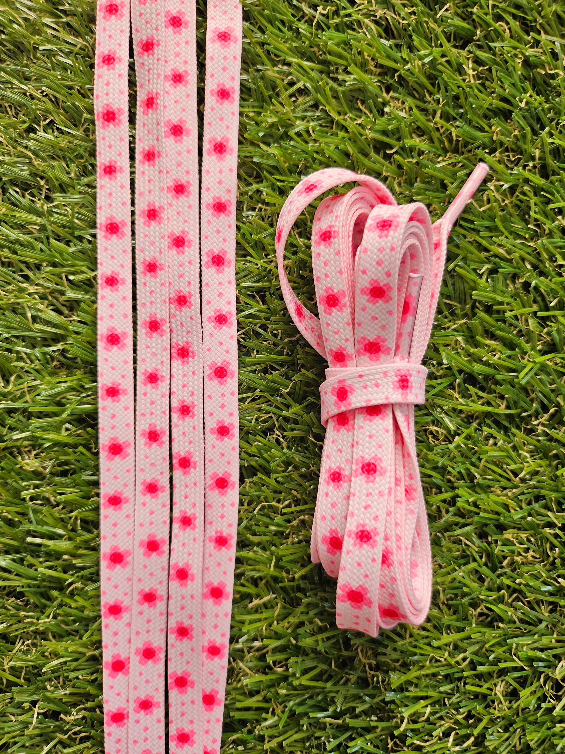 Pink shoelaces with pink flowers on a grass background