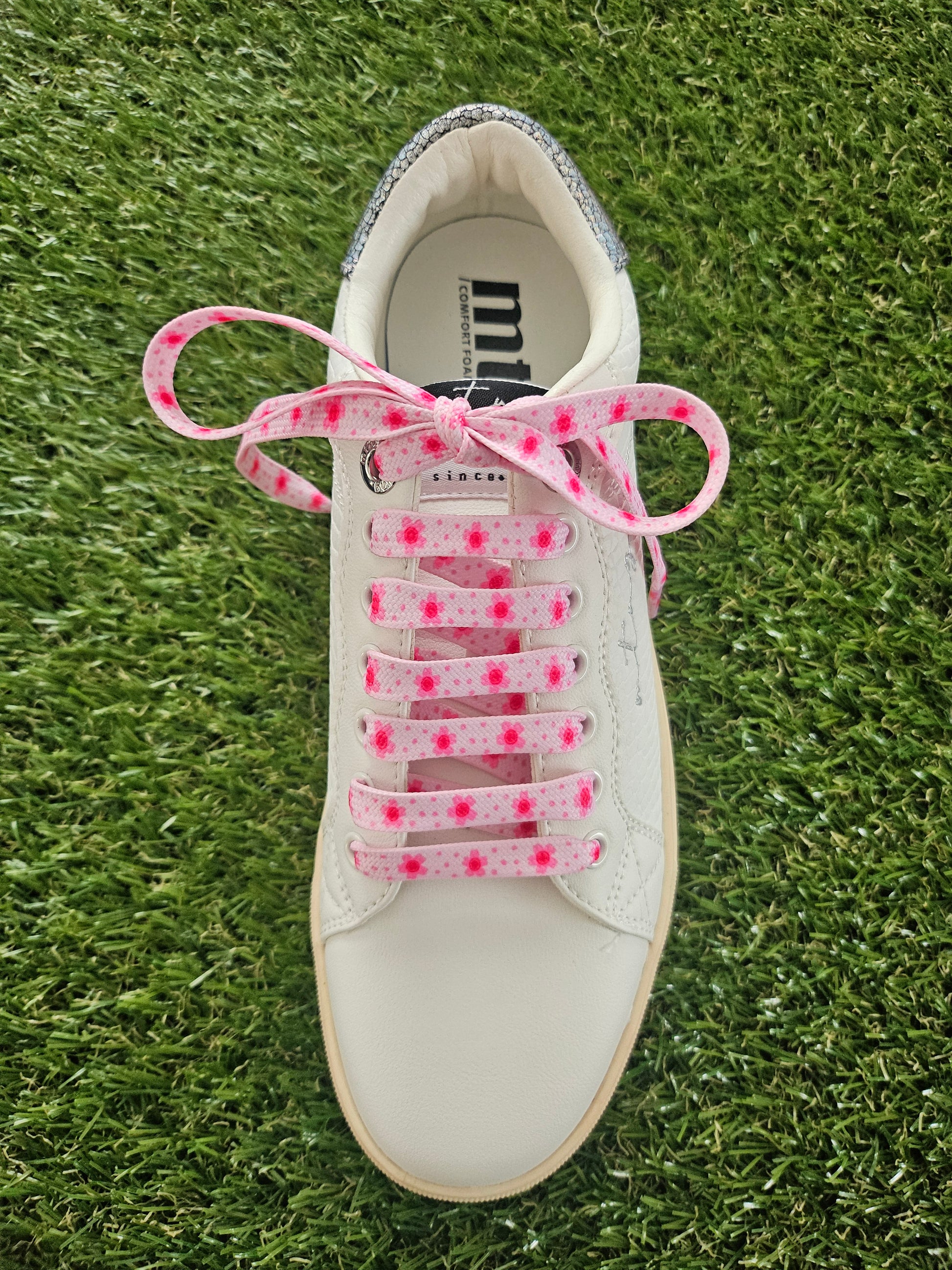 White sneaker with pink shoelaces on a grass background