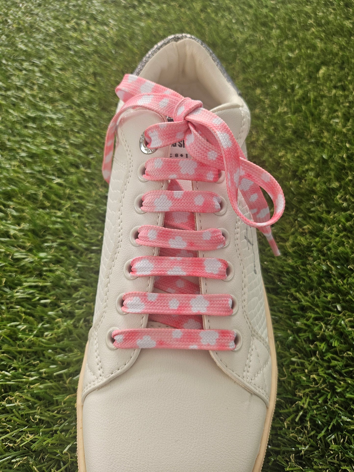 White sneaker with pink cloud shoelaces on a grass background