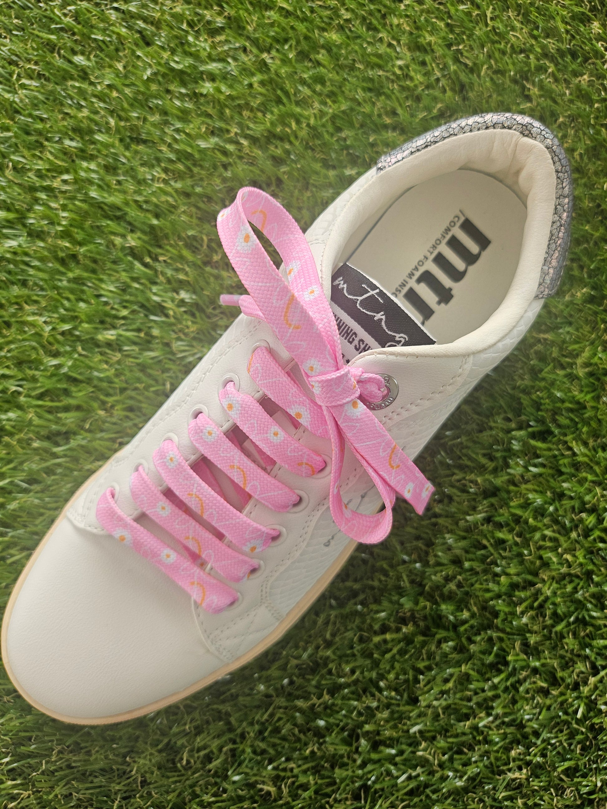 White sneaker with pink floral laces on grass