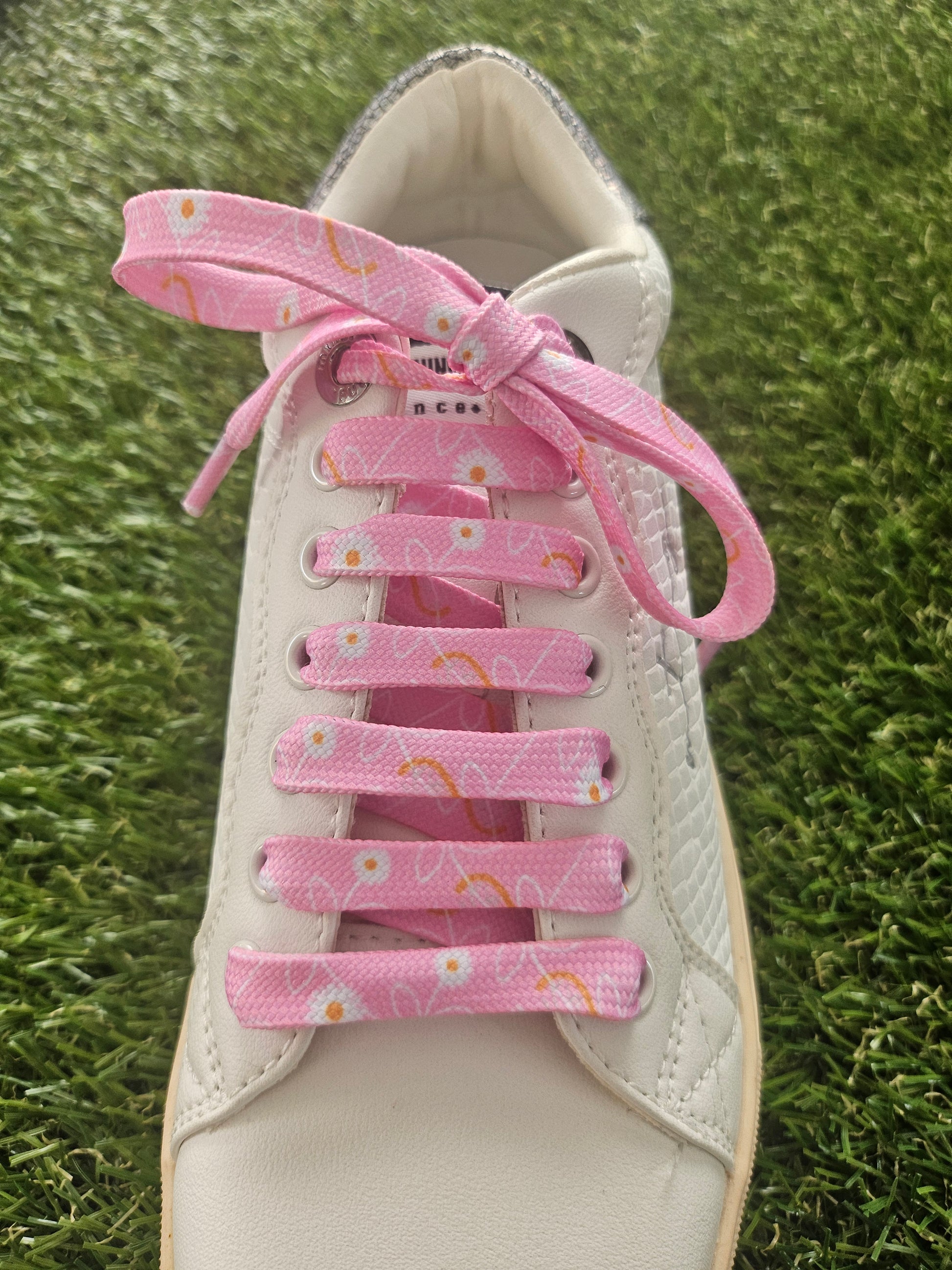 White sneaker with pink shoelaces on a grass background