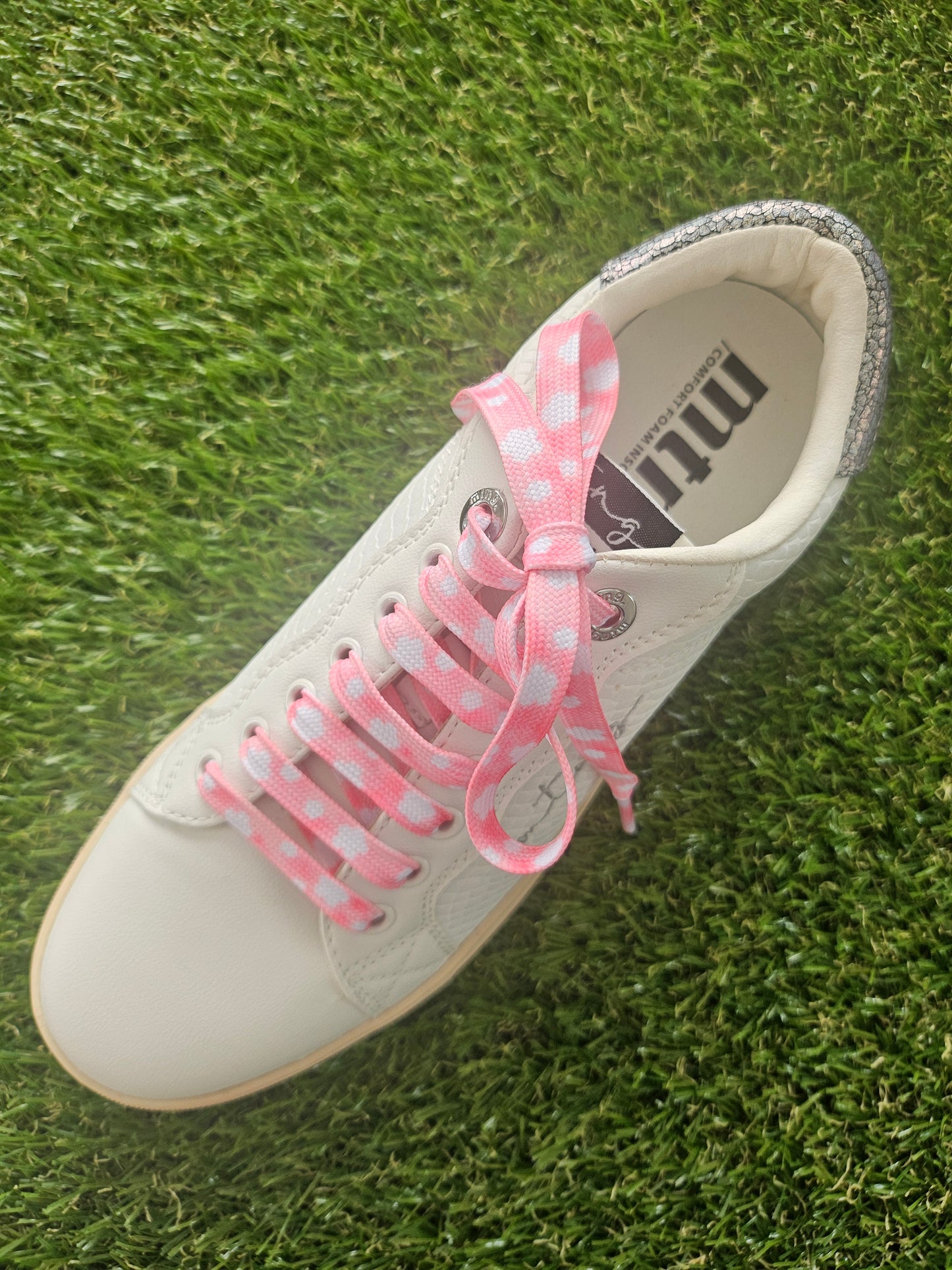 White sneaker with pink laces with white coloured clouds laces on grass