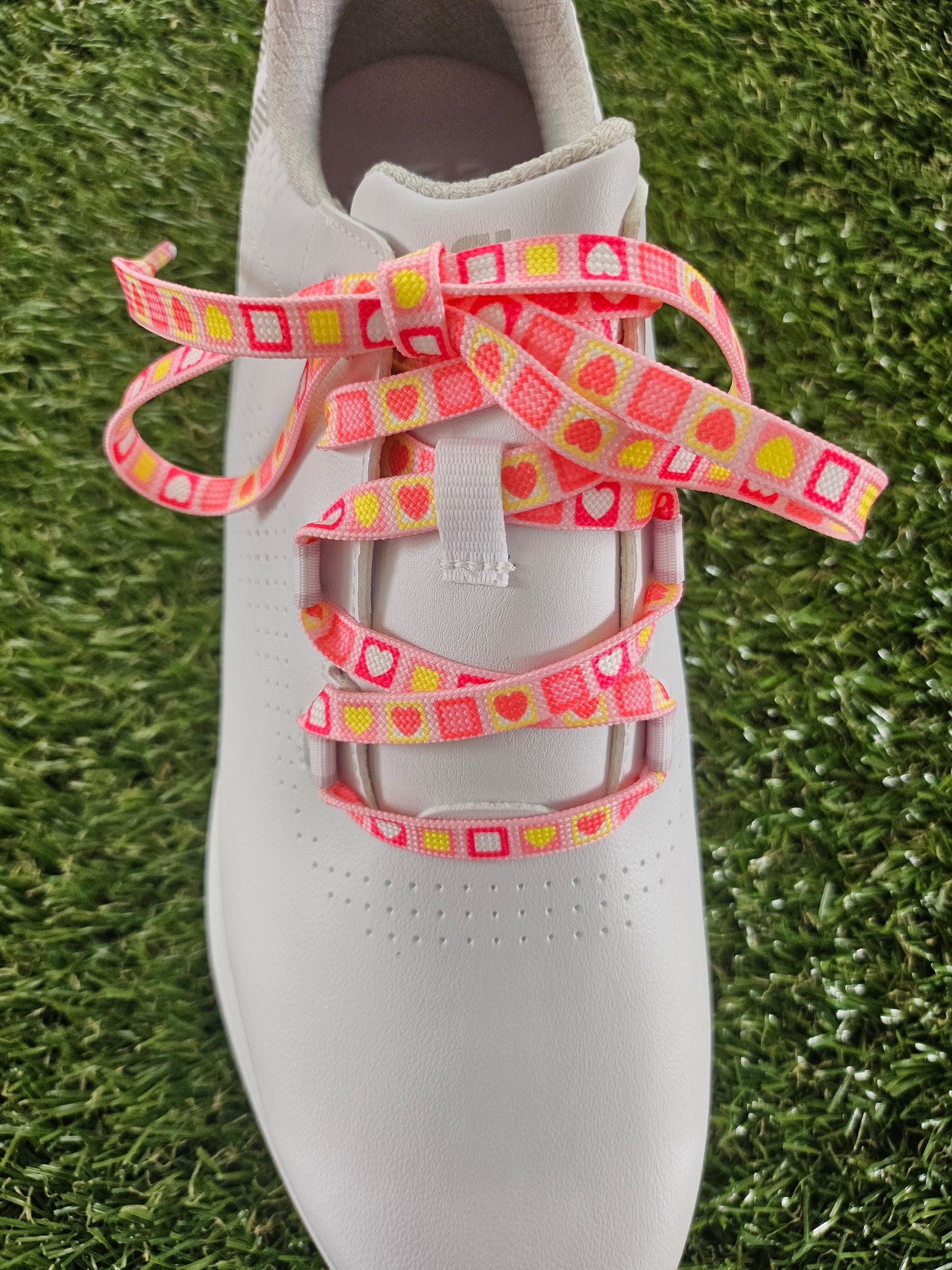 White womans golf shoe with pink and yellow patterned laces on a grass background
