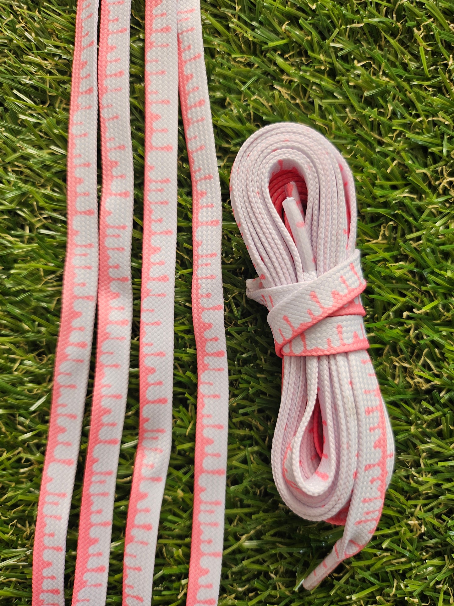 White shoelaces with pink accents on a grass background