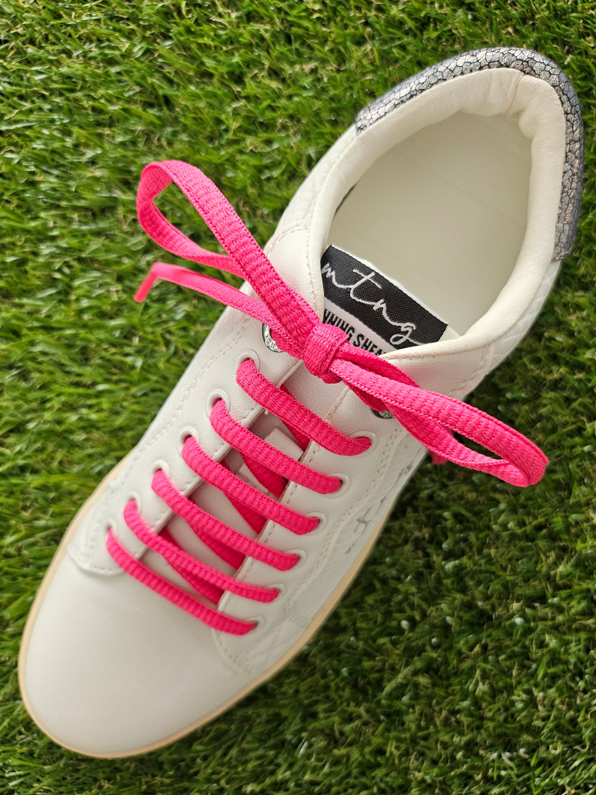 white trainers with hot pink laces on grass