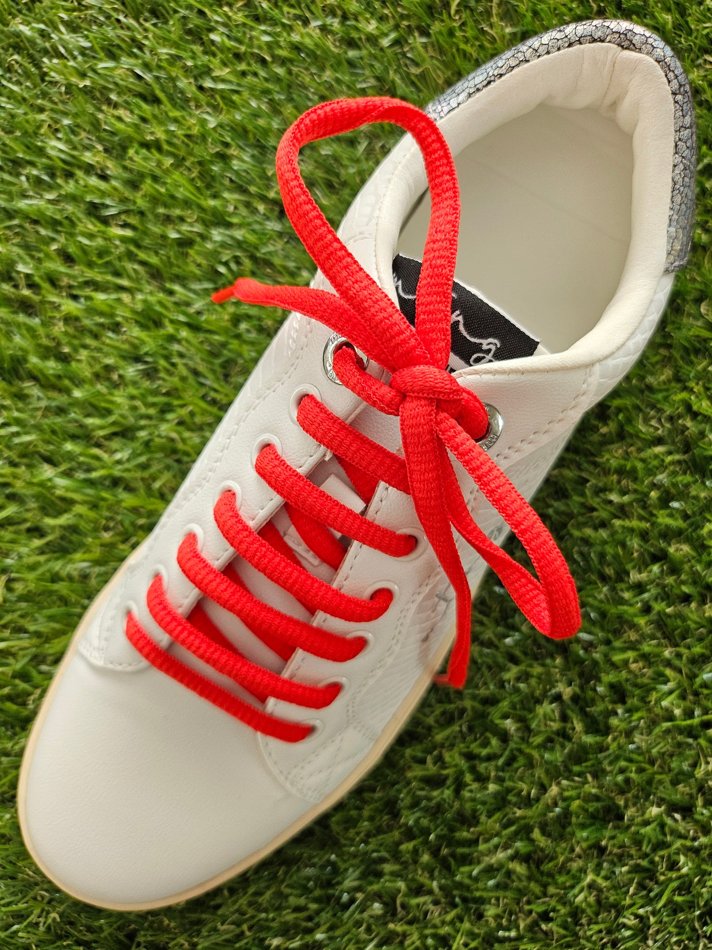 White sneaker with red laces on grass