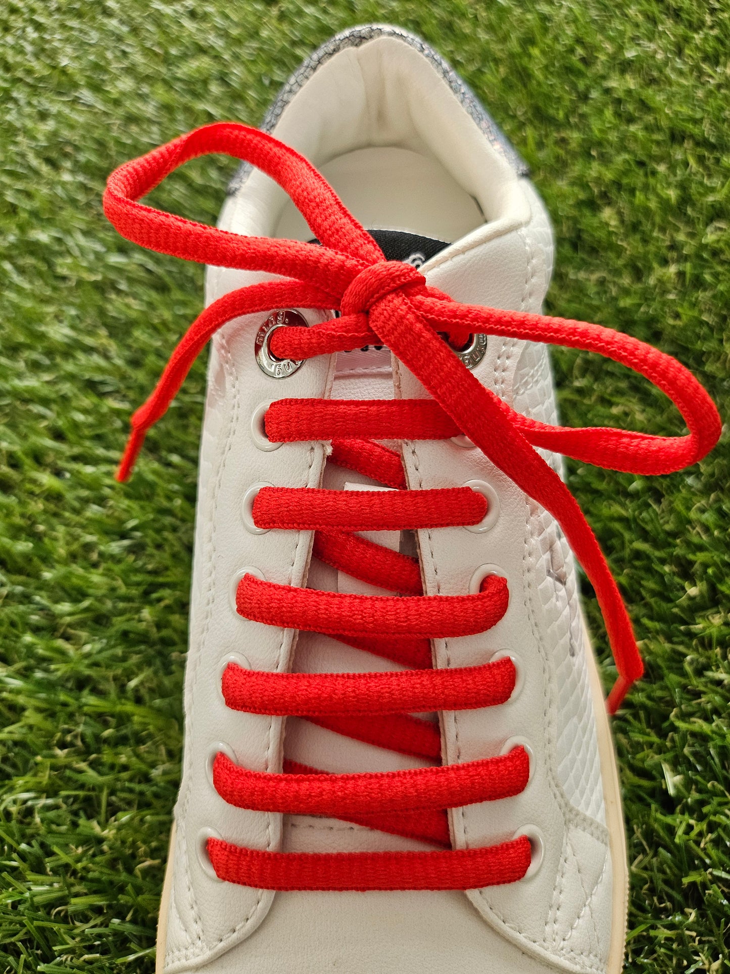 White sneaker with red laces on a grass background