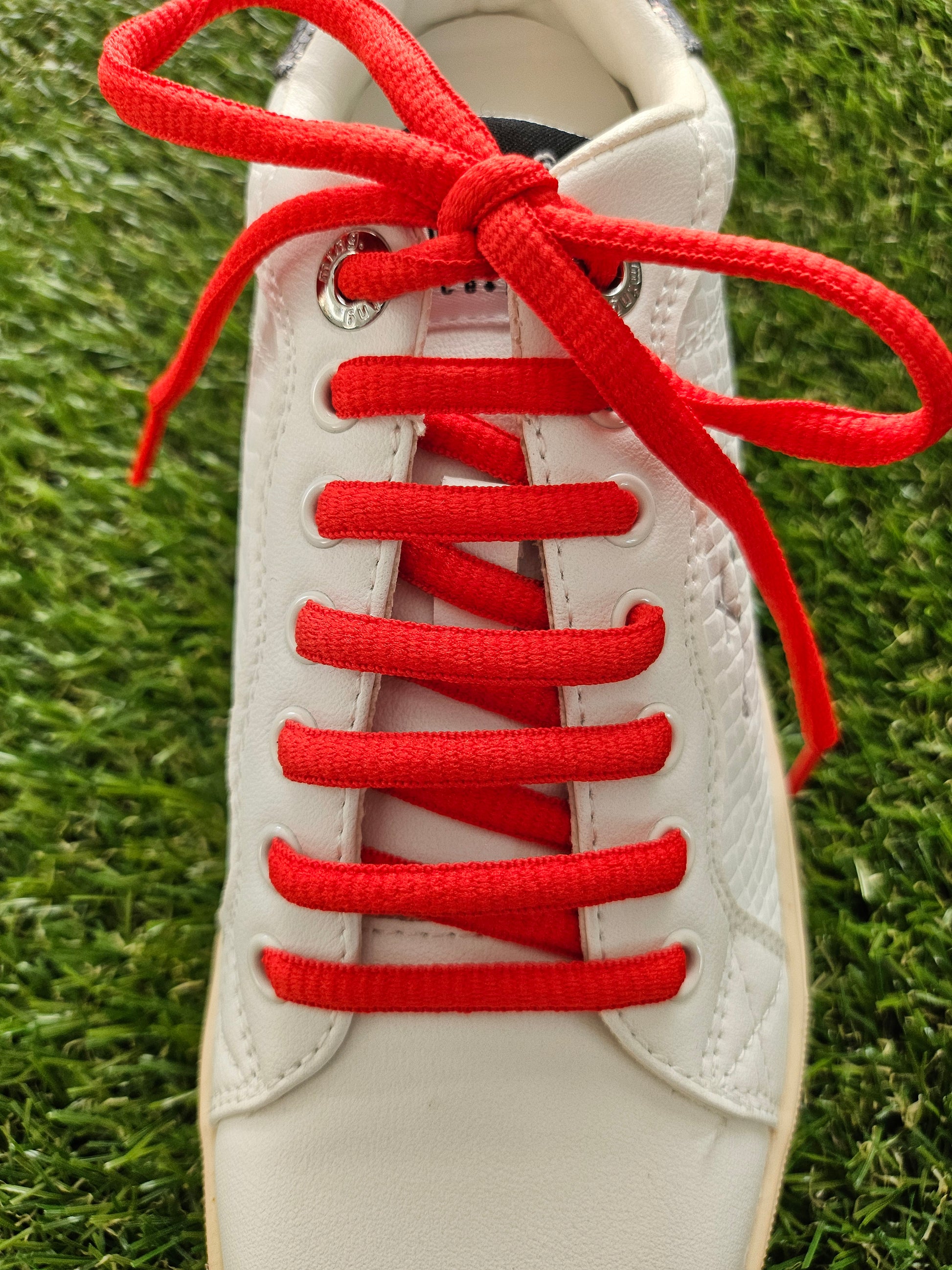 red shoelaces on white trainer on grass