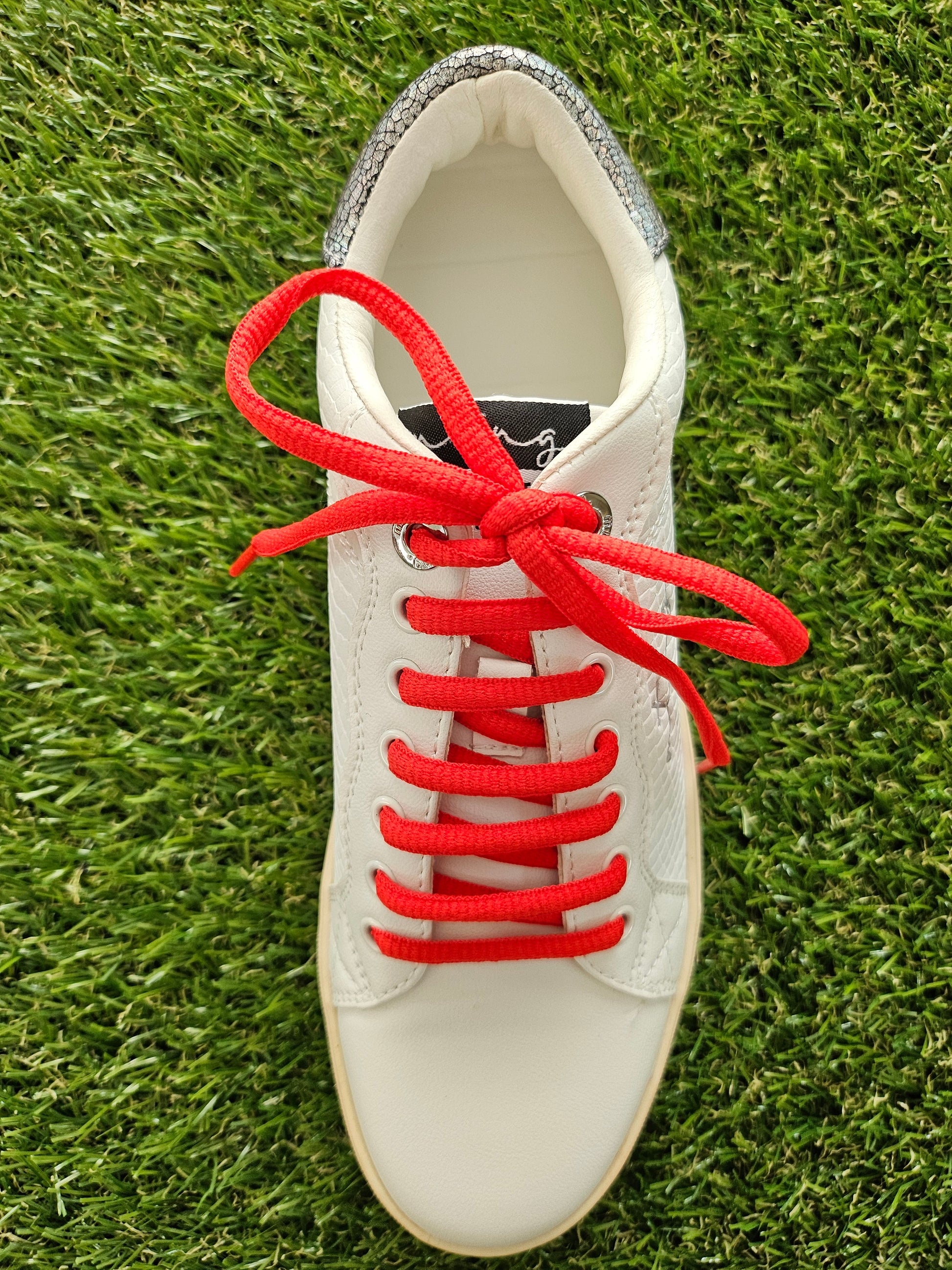 red shoelaces on white trainer on grass