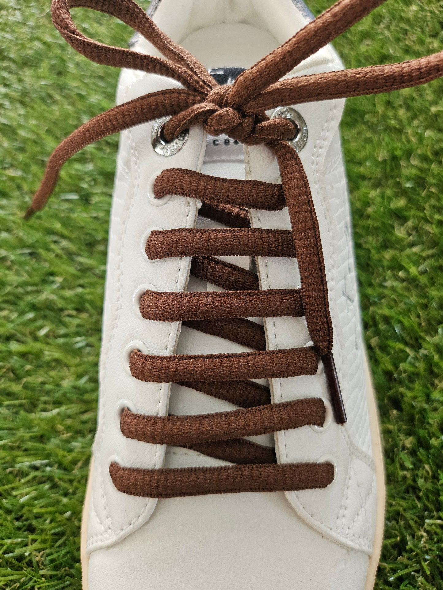 White sneaker with brown laces on a grass background