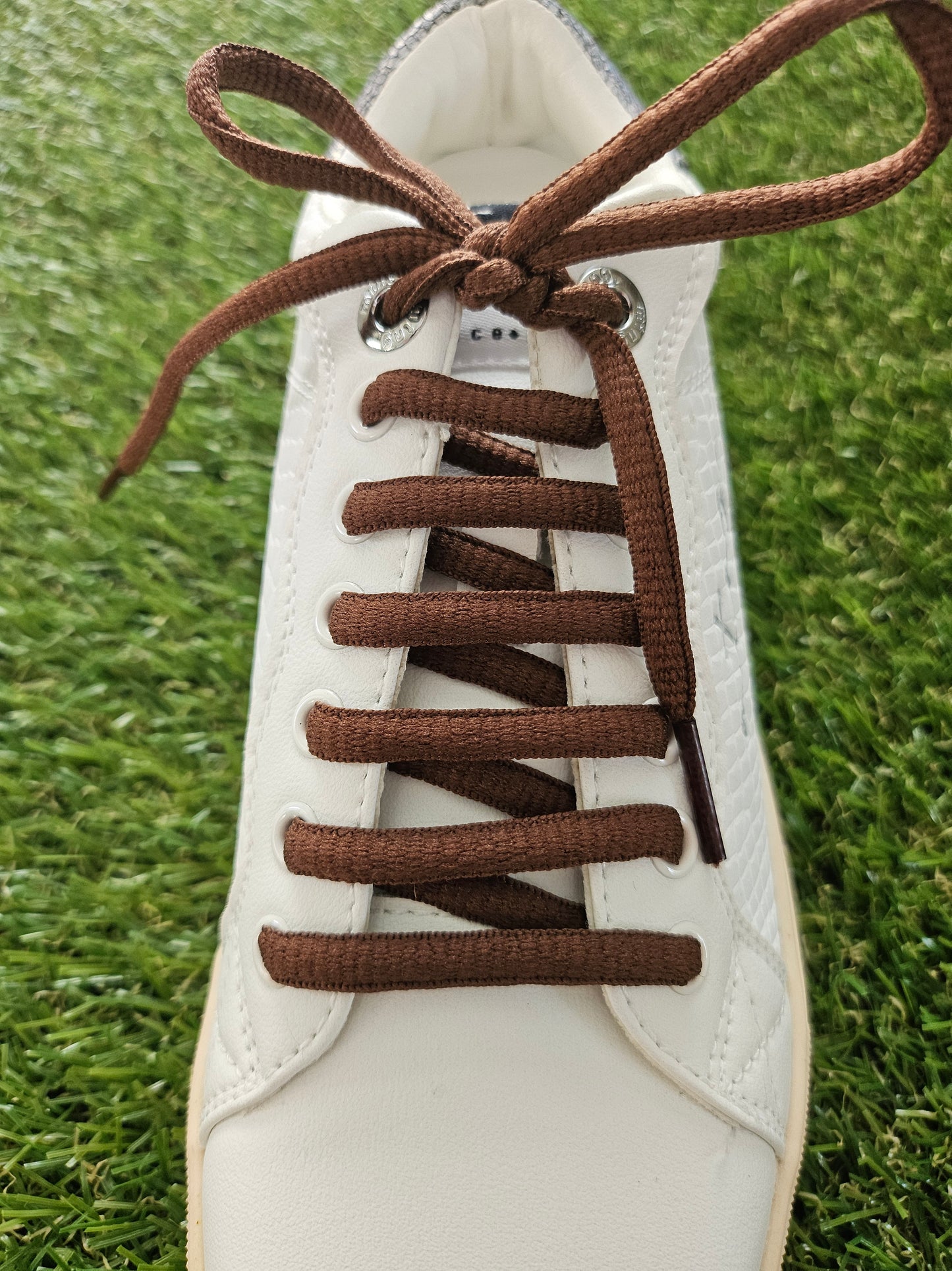 White sneaker with brown laces on a grass background