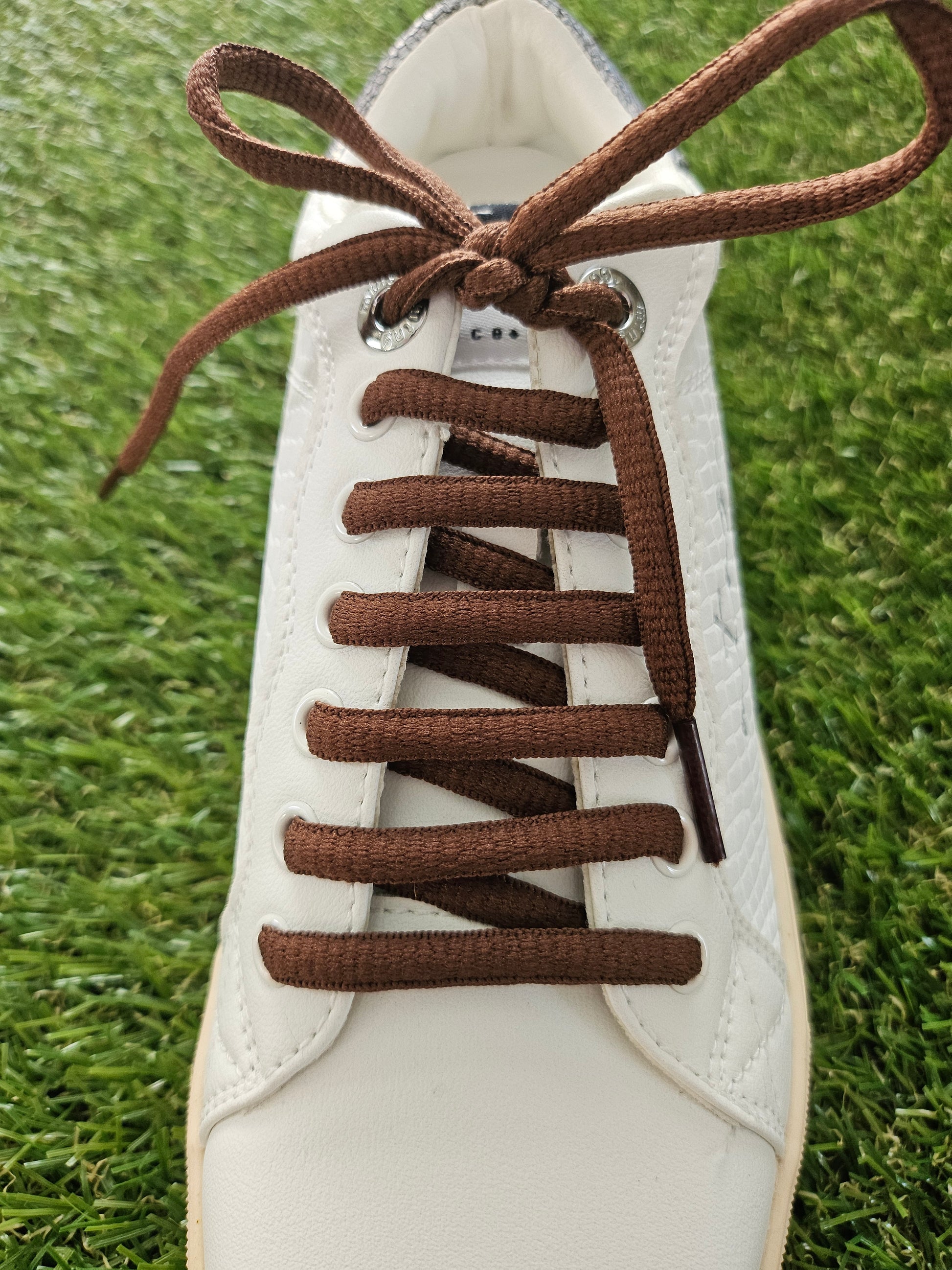 White sneaker with brown laces on a grass background