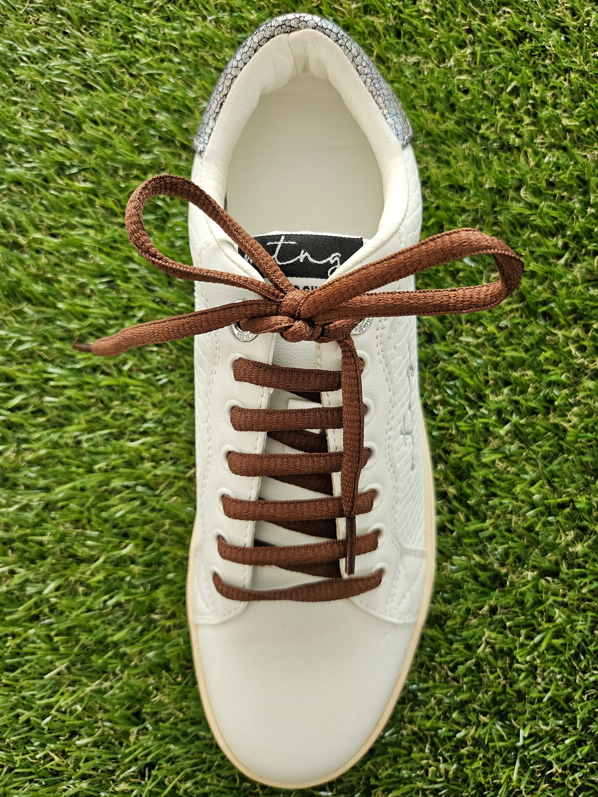 White sneaker with brown laces on a grass background