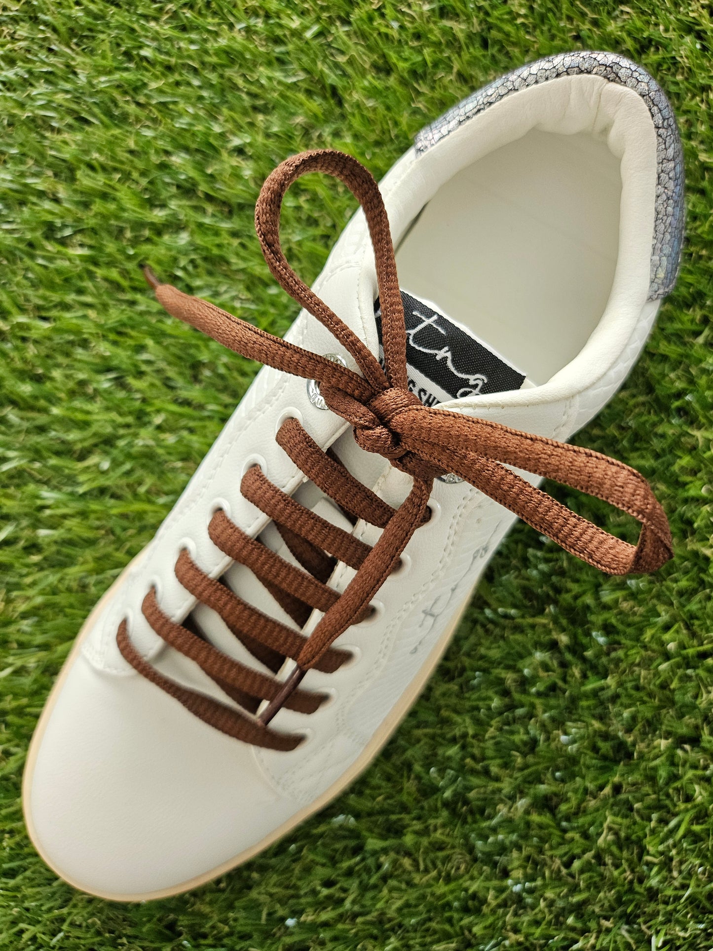 White sneaker with brown laces on a grass background
