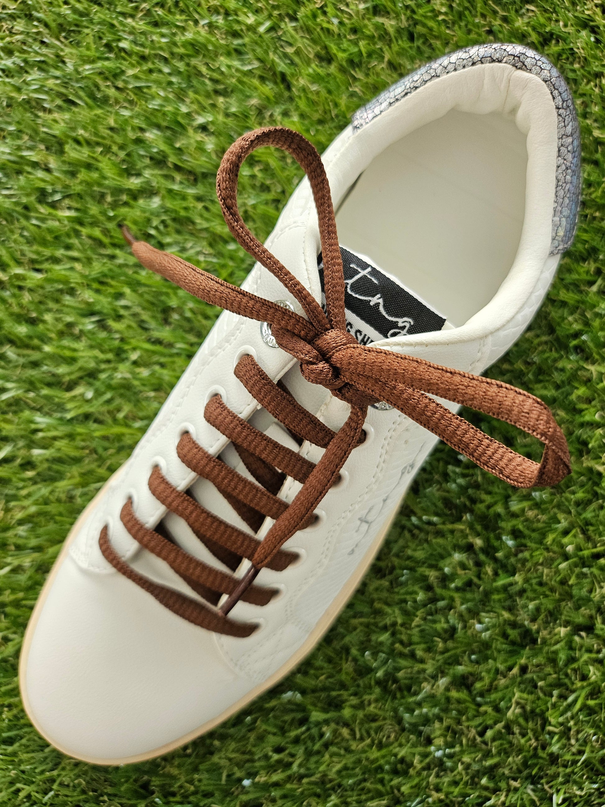 White sneaker with brown laces on a grass background