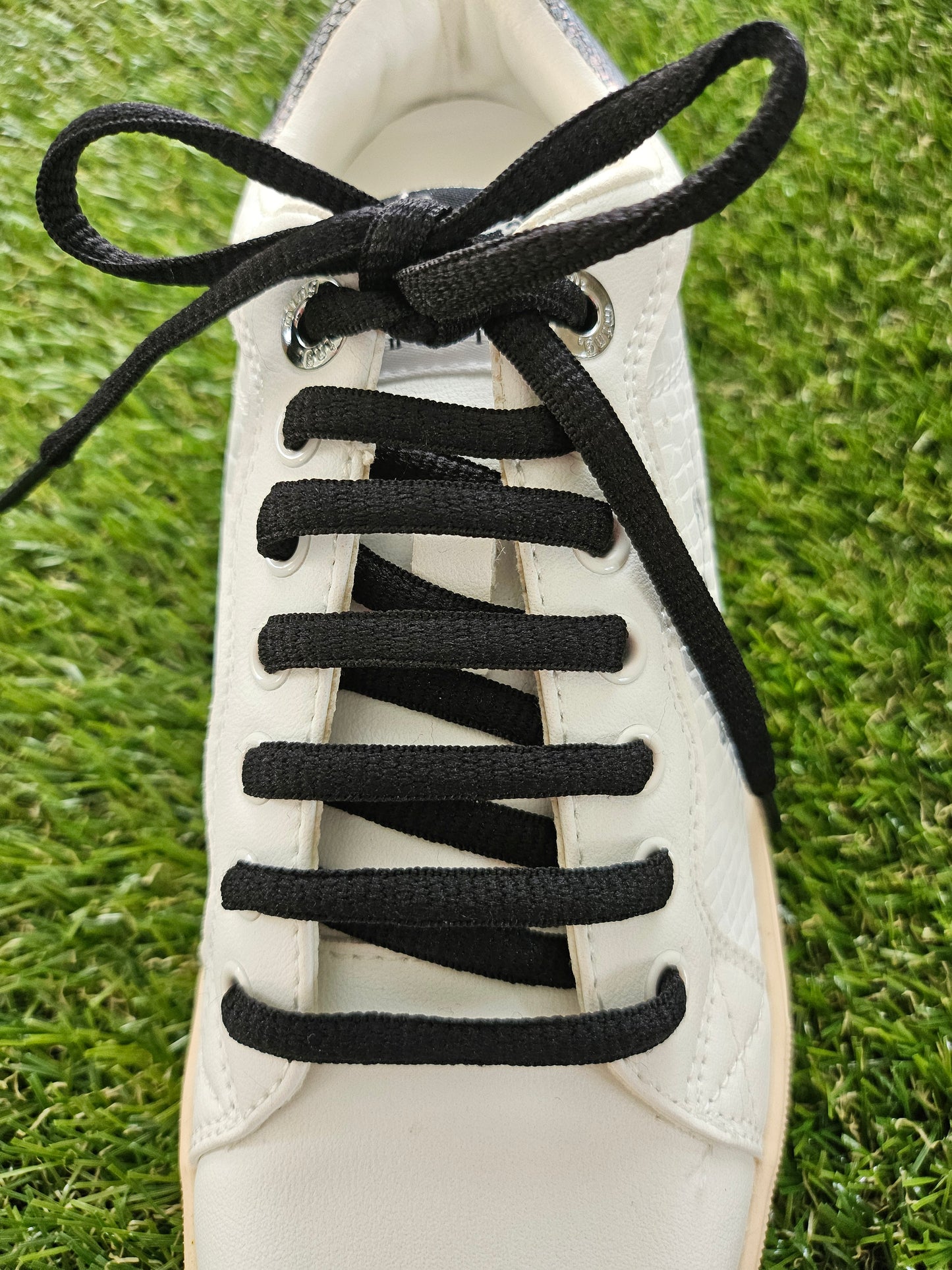 White sneaker with black shoelaces on a grass background