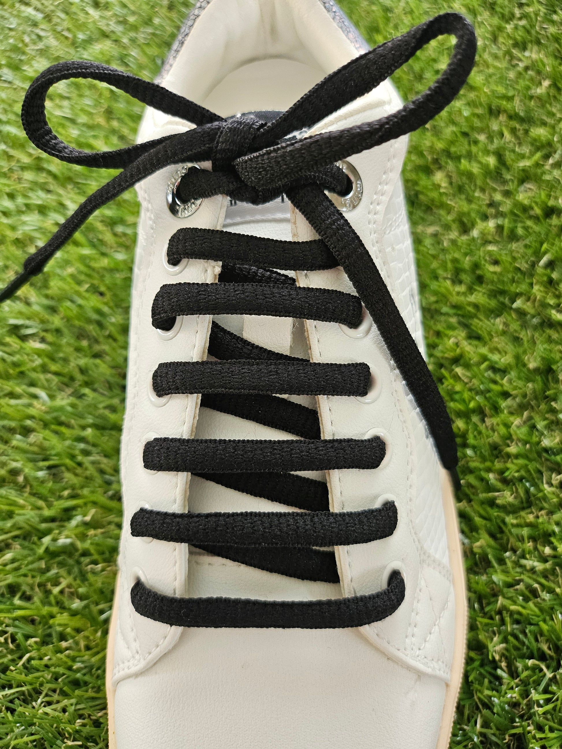 White sneaker with black shoelaces on a grass background