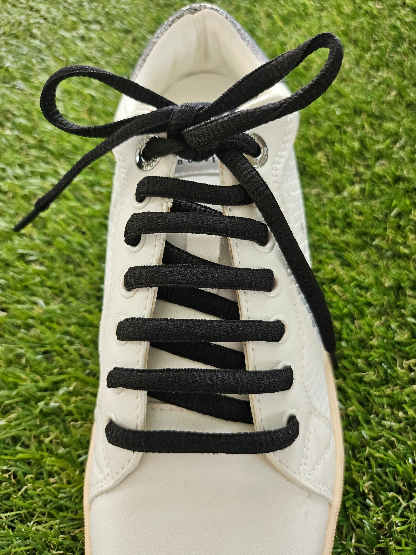 White sneaker with black elastic laces on a grass background