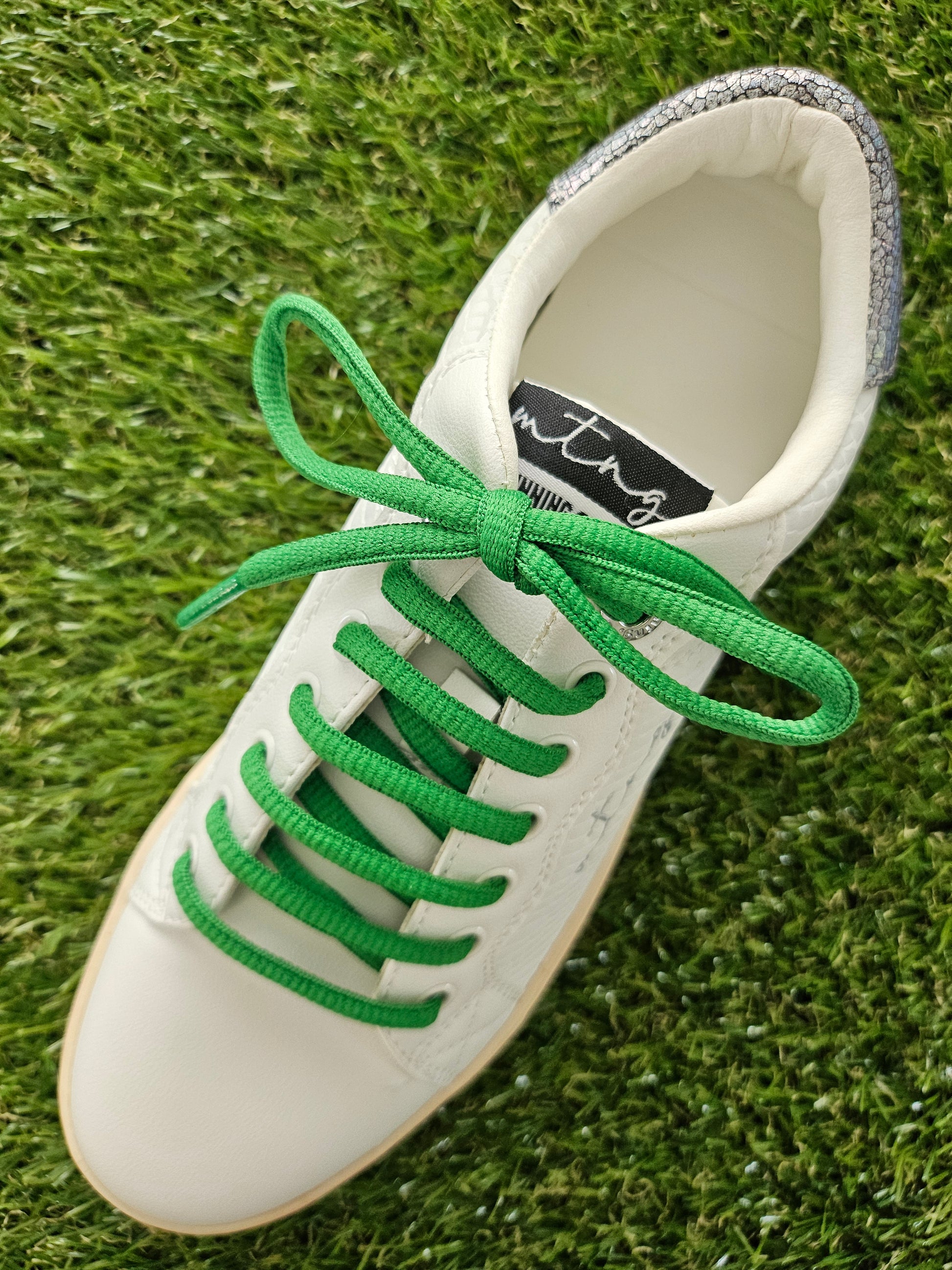 green shoelaces on white trainer on grass