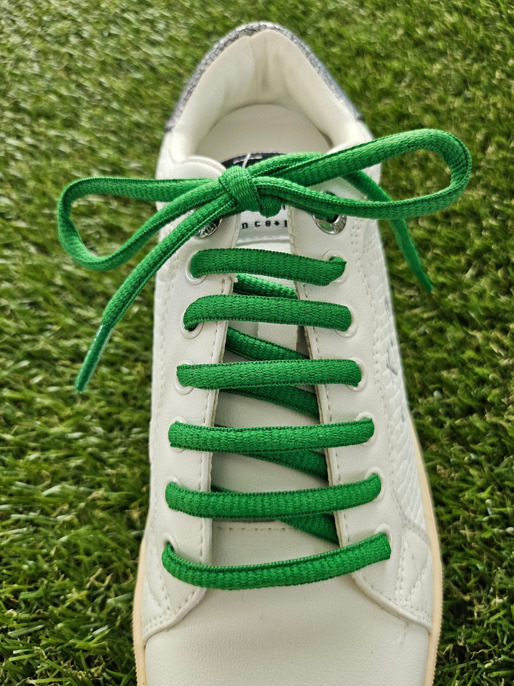green shoelaces on white trainer on grass background
