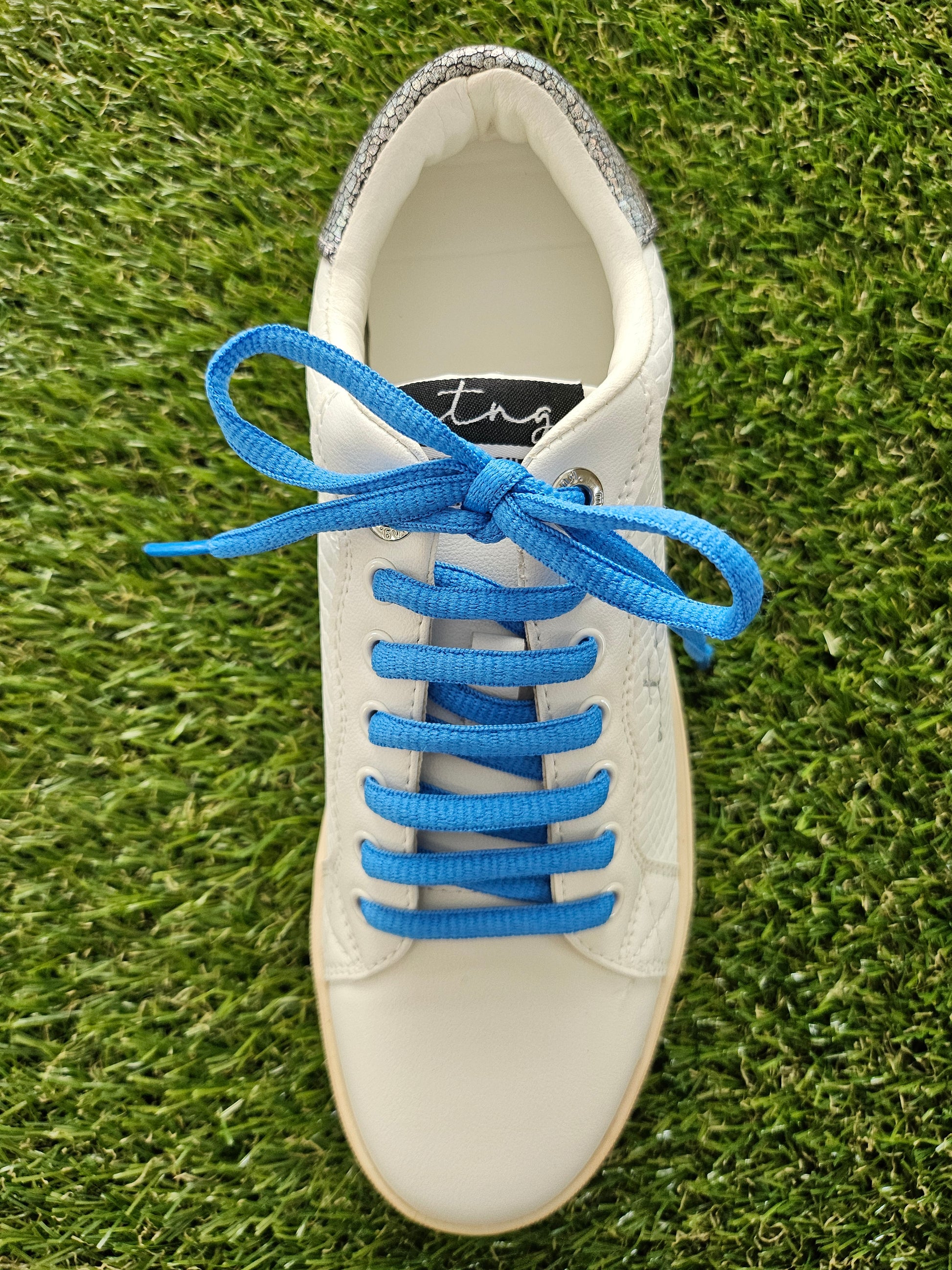 White sneaker with blue laces on a grass background