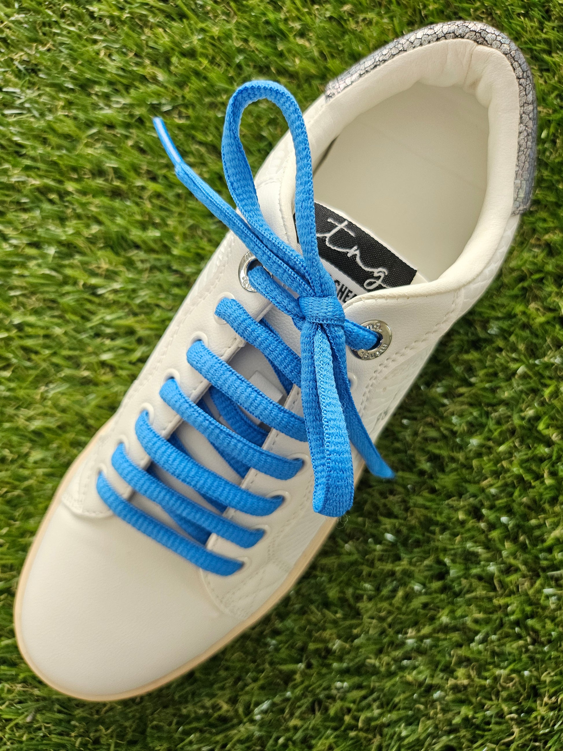 White sneaker with blue laces on a grass background