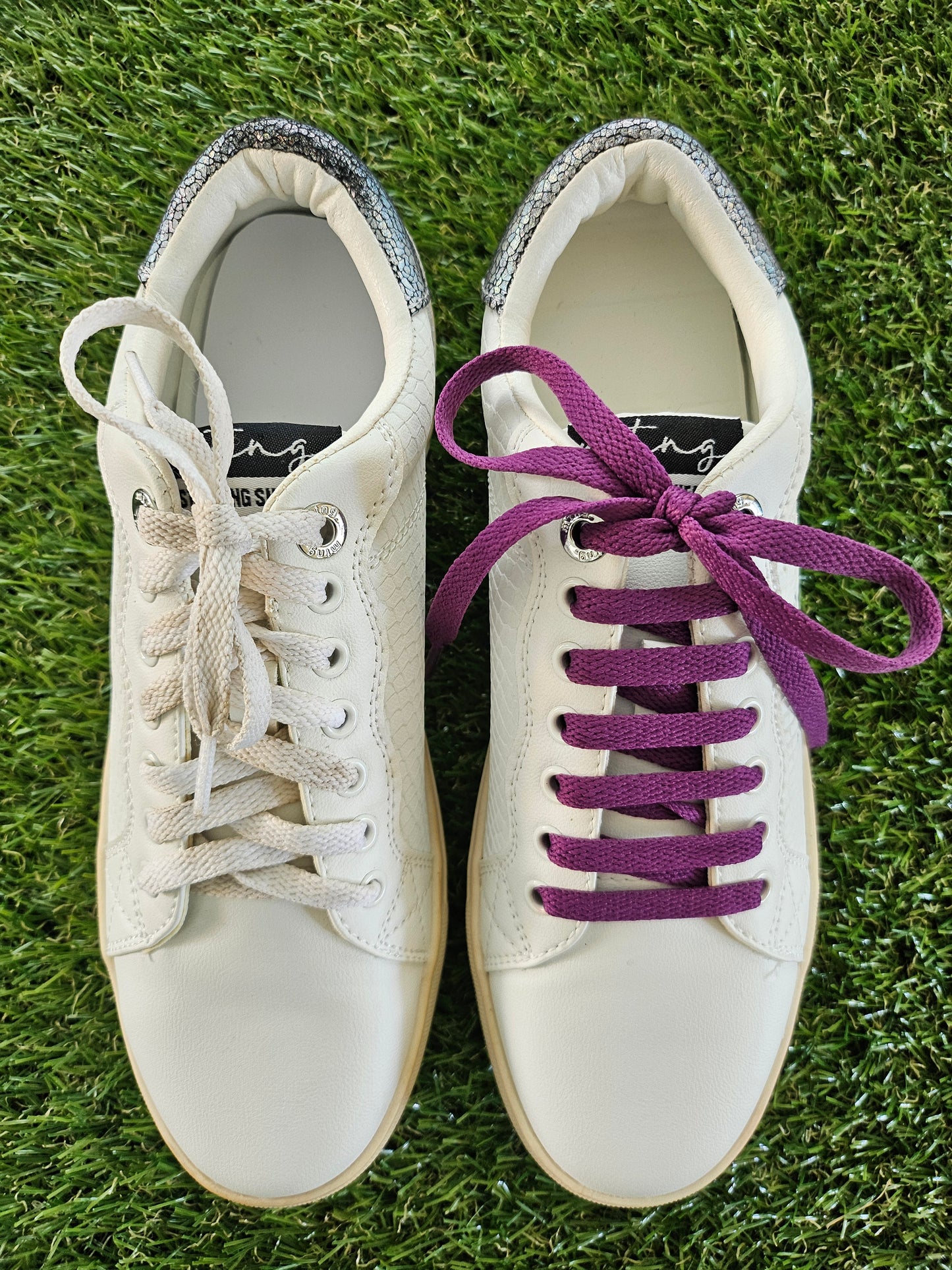 White sneakers with purple laces on a grass background