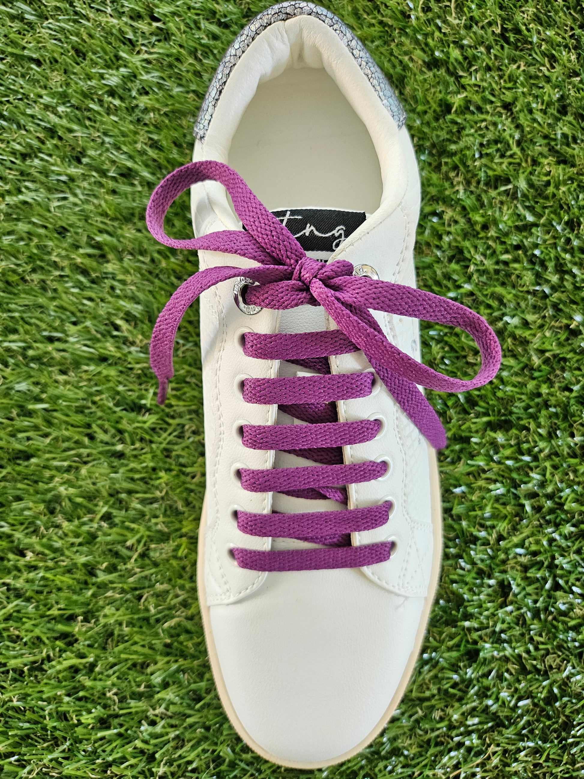 White sneaker with purple laces on a grass background