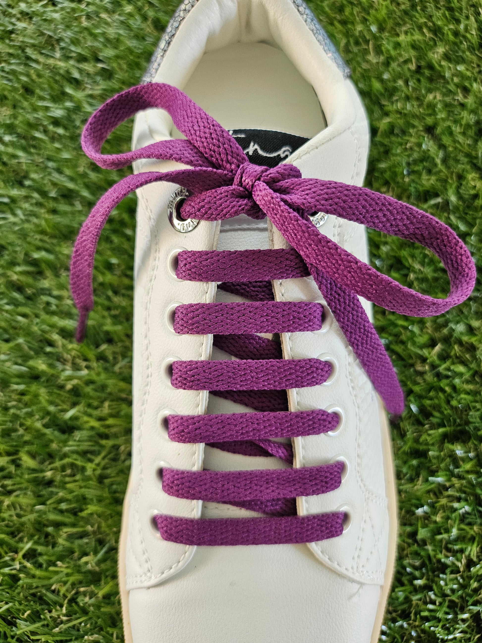 White sneaker with purple laces on a grass background