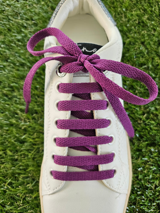 White sneaker with purple laces on a grass background
