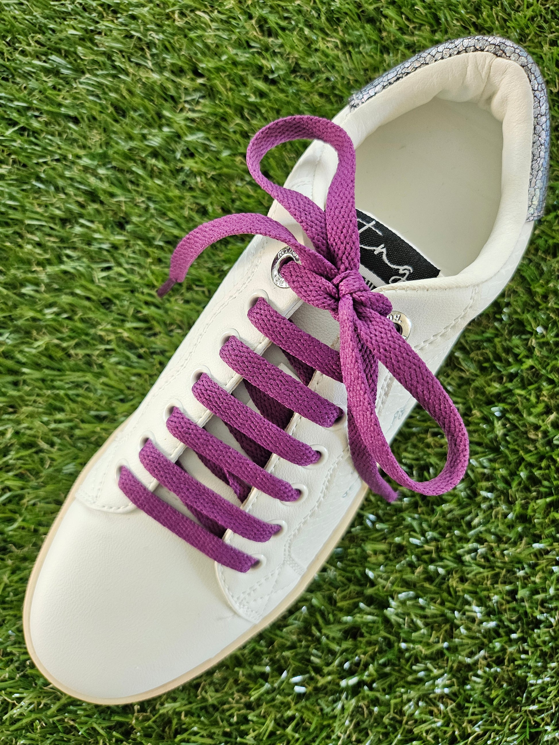 White sneaker with purple laces on a grass background