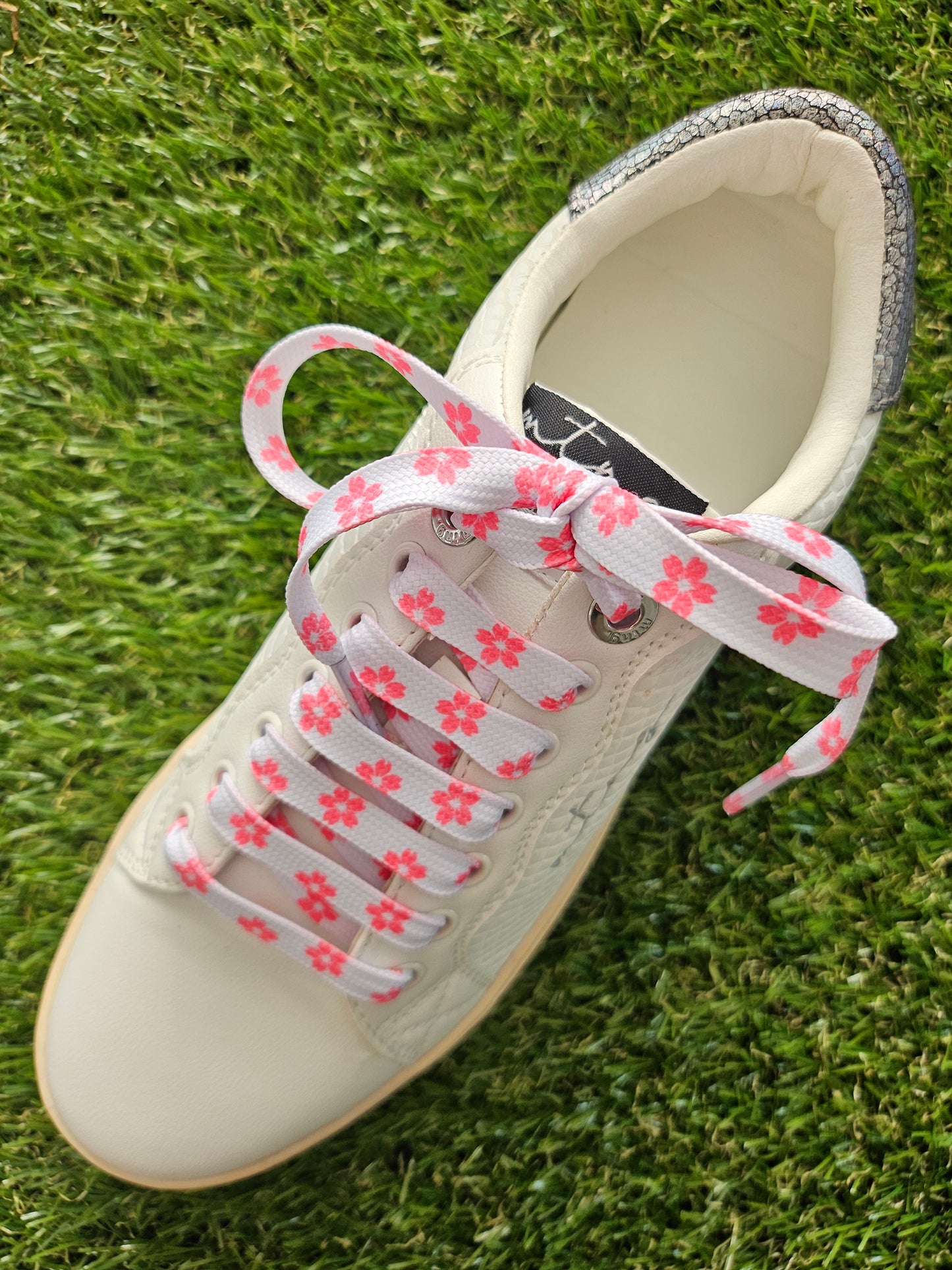 White sneaker with floral-patterned laces on a grass background