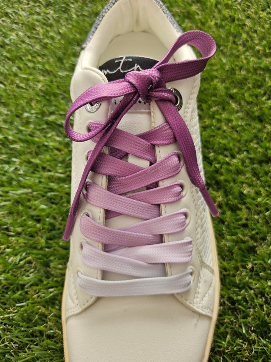 White sneaker with purple and pink laces on a grass background