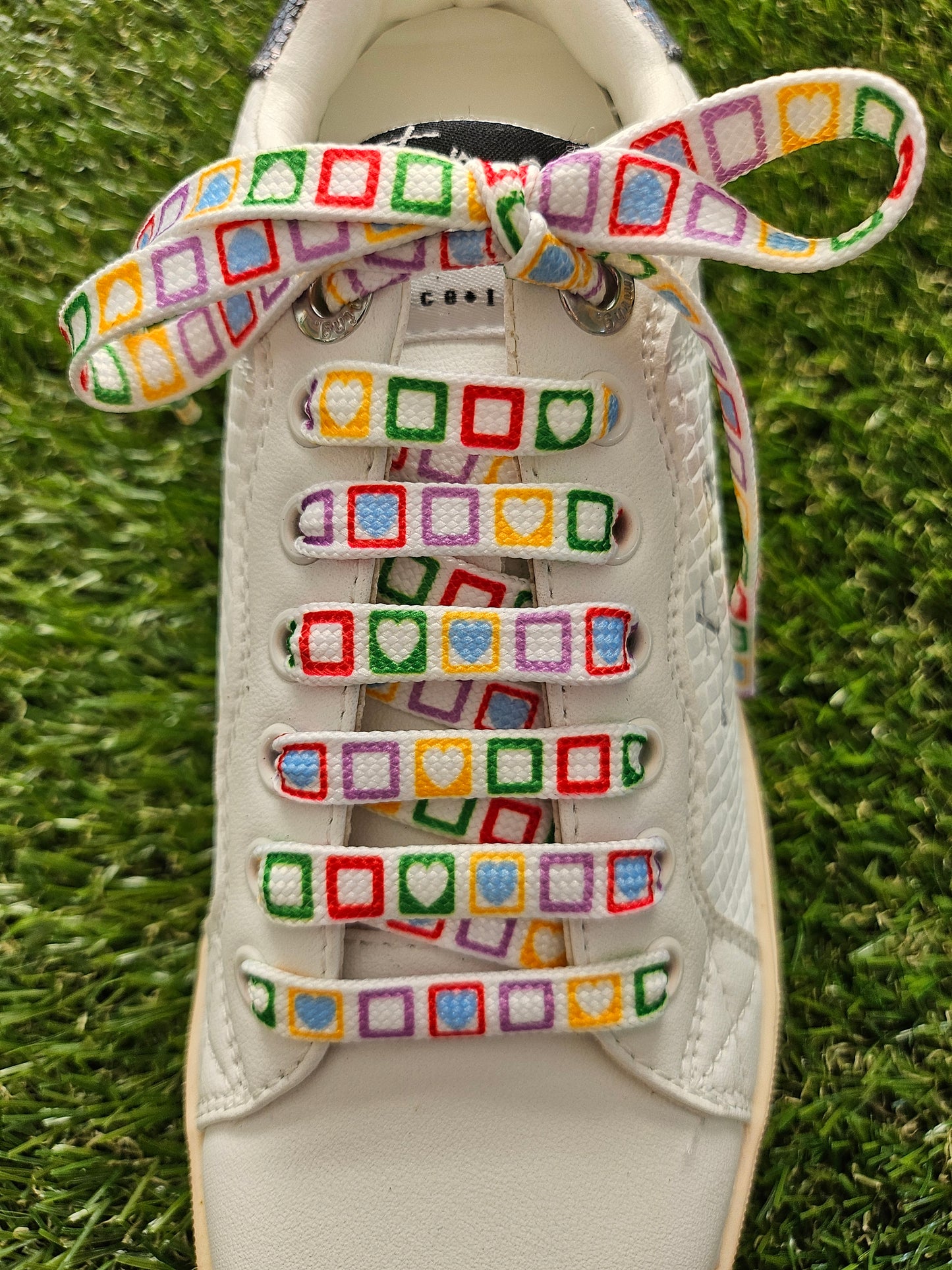 White sneaker with colorful patterned laces on a grass background