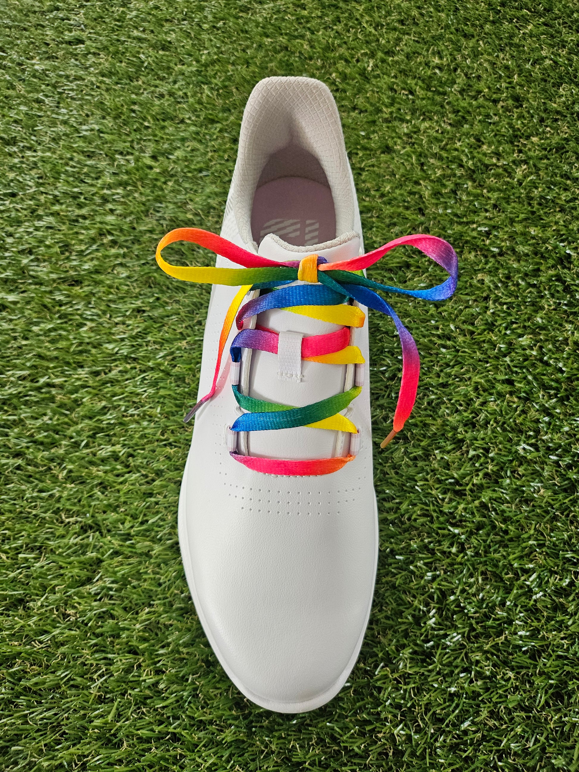White golf shoe with rainbow shoelaces on grass