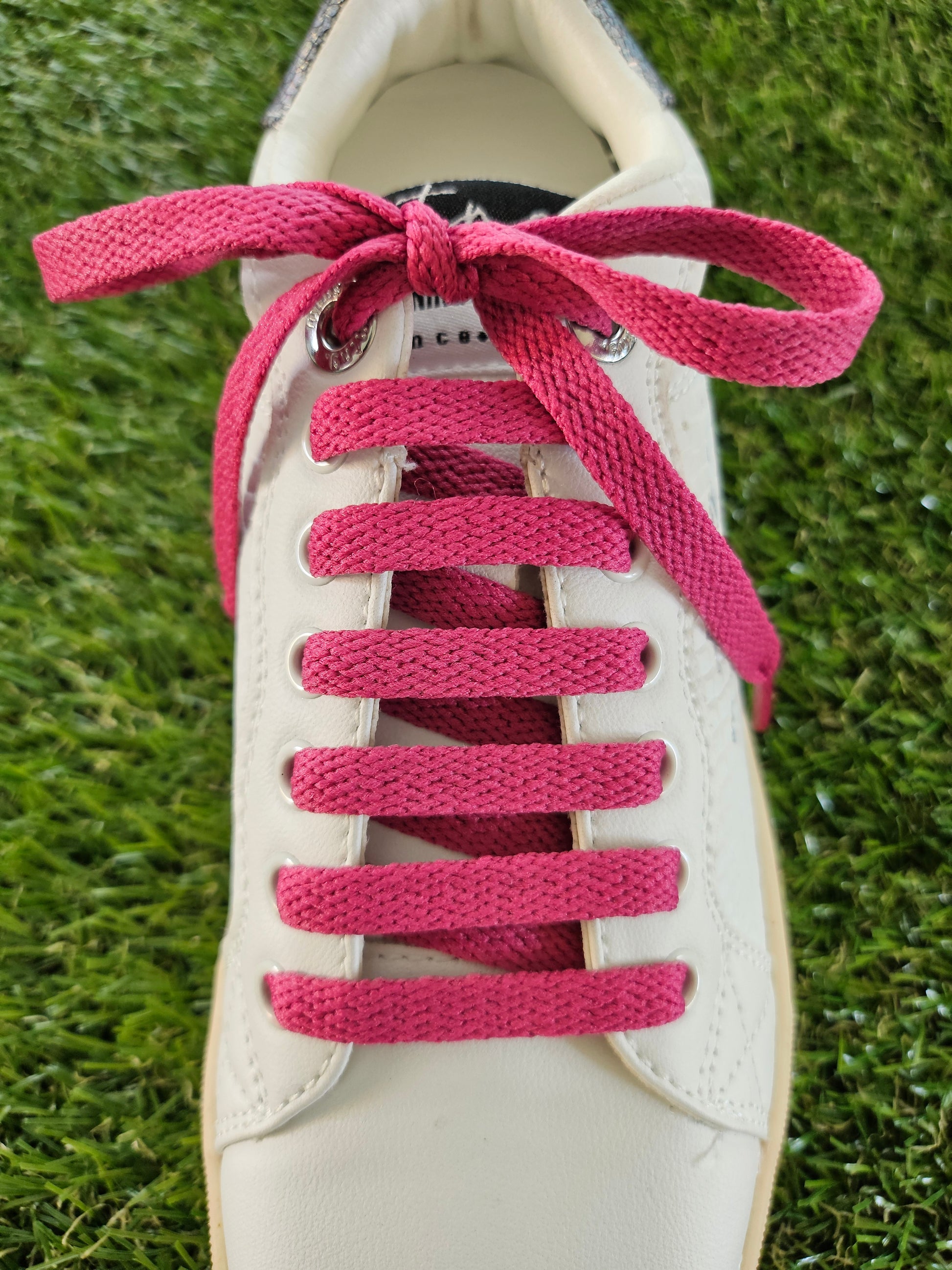 raspberry pink shoelaces in a white trainer on green grass